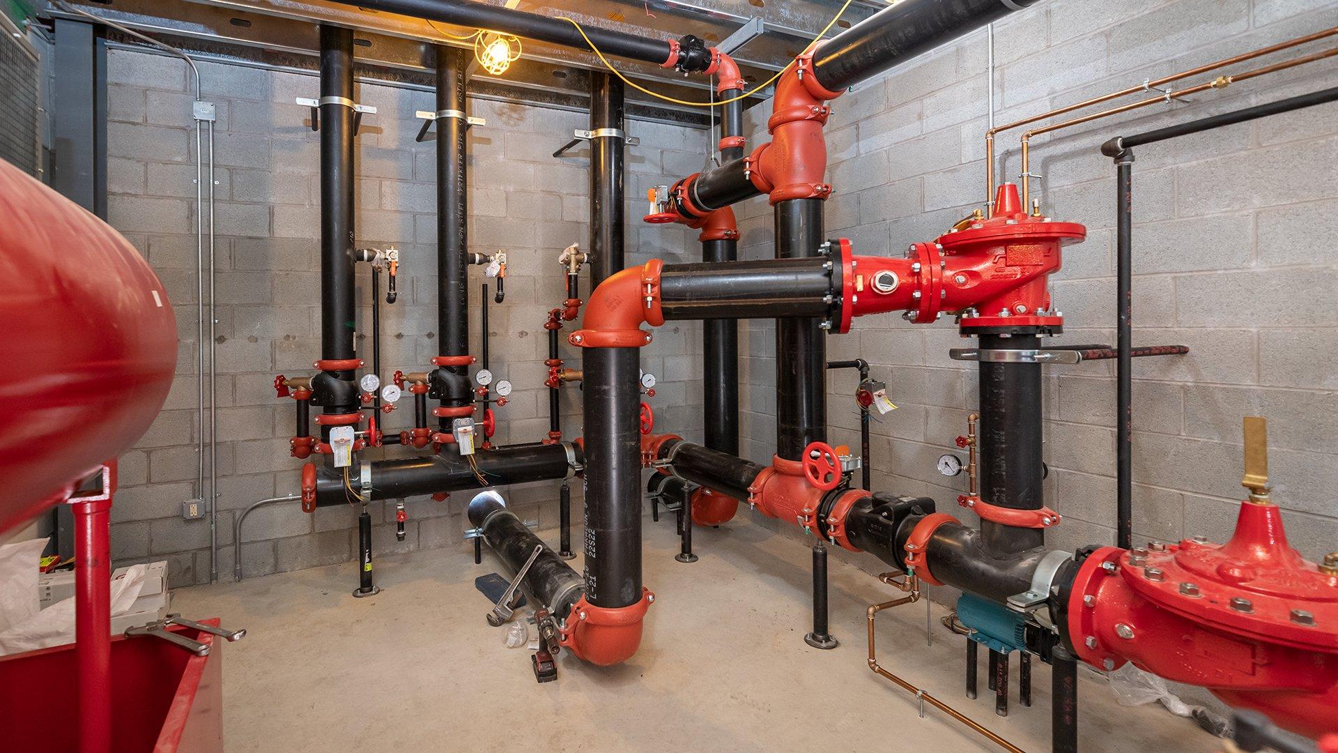 A fire sprinkler room with red and black pipe and valves.