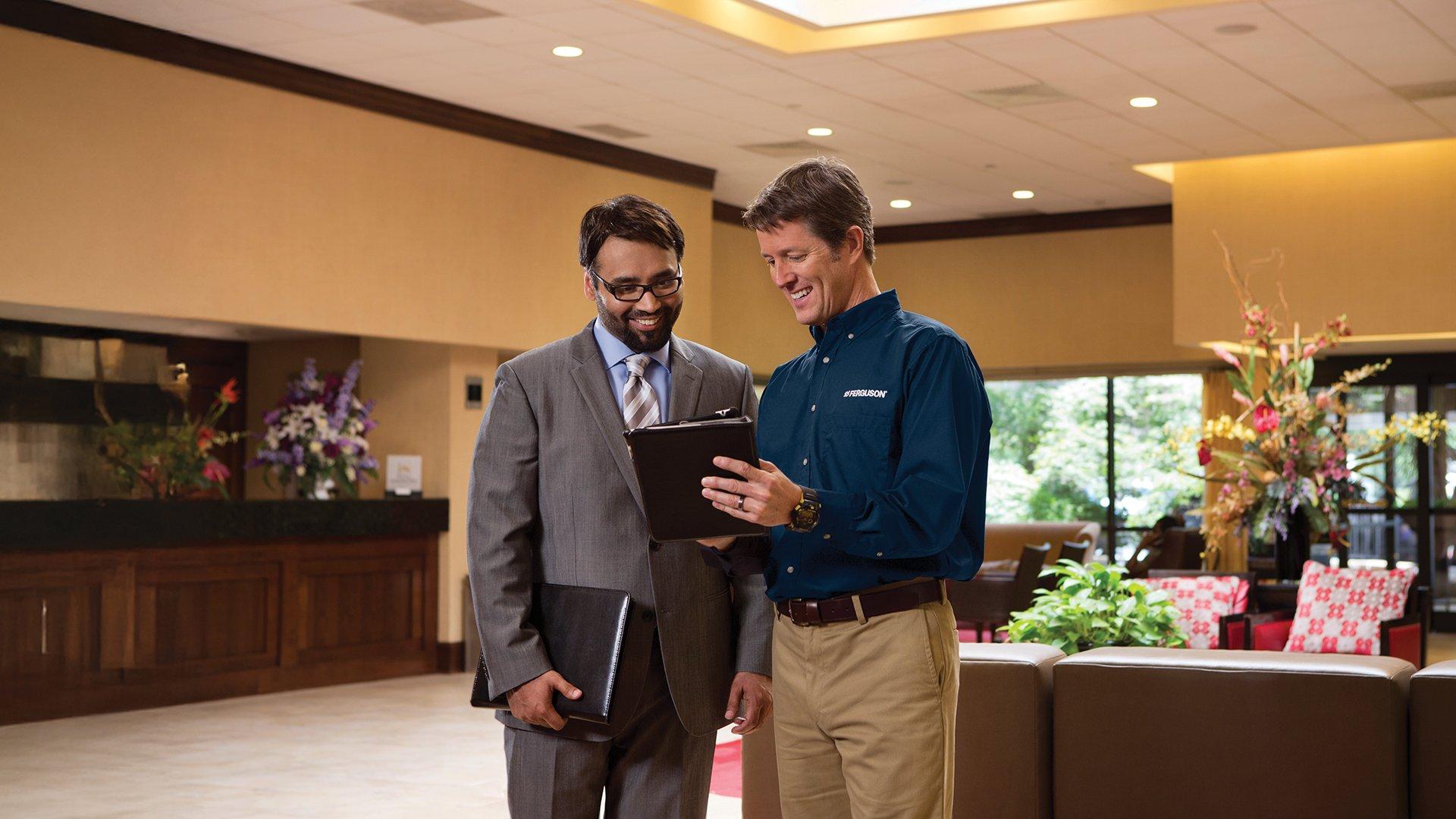Two gentleman looking at iPad in what looks like a hotel or commercial lobby space.