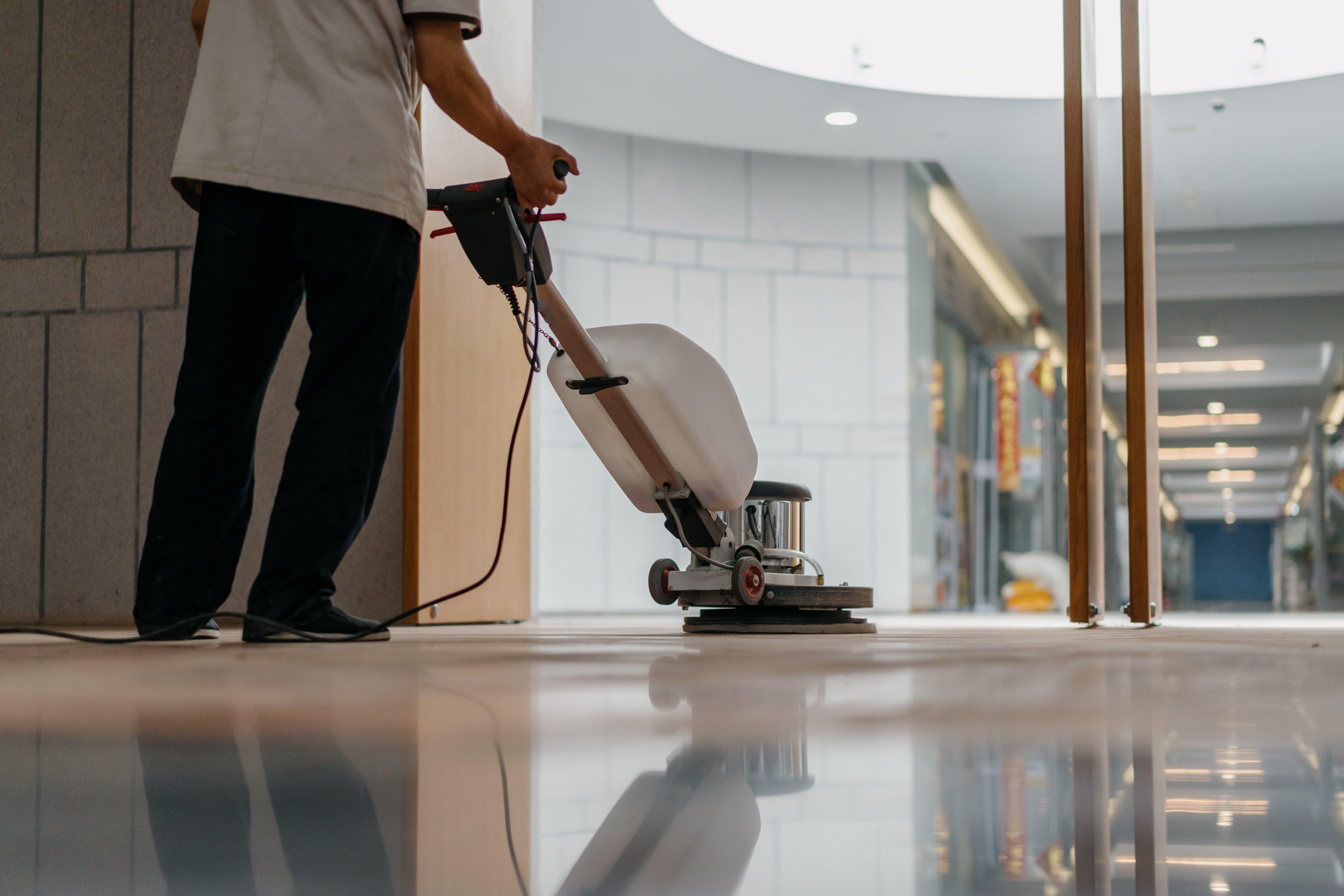 A facilities worker cleans the floor in a commercial building lobby with a floor buffer.