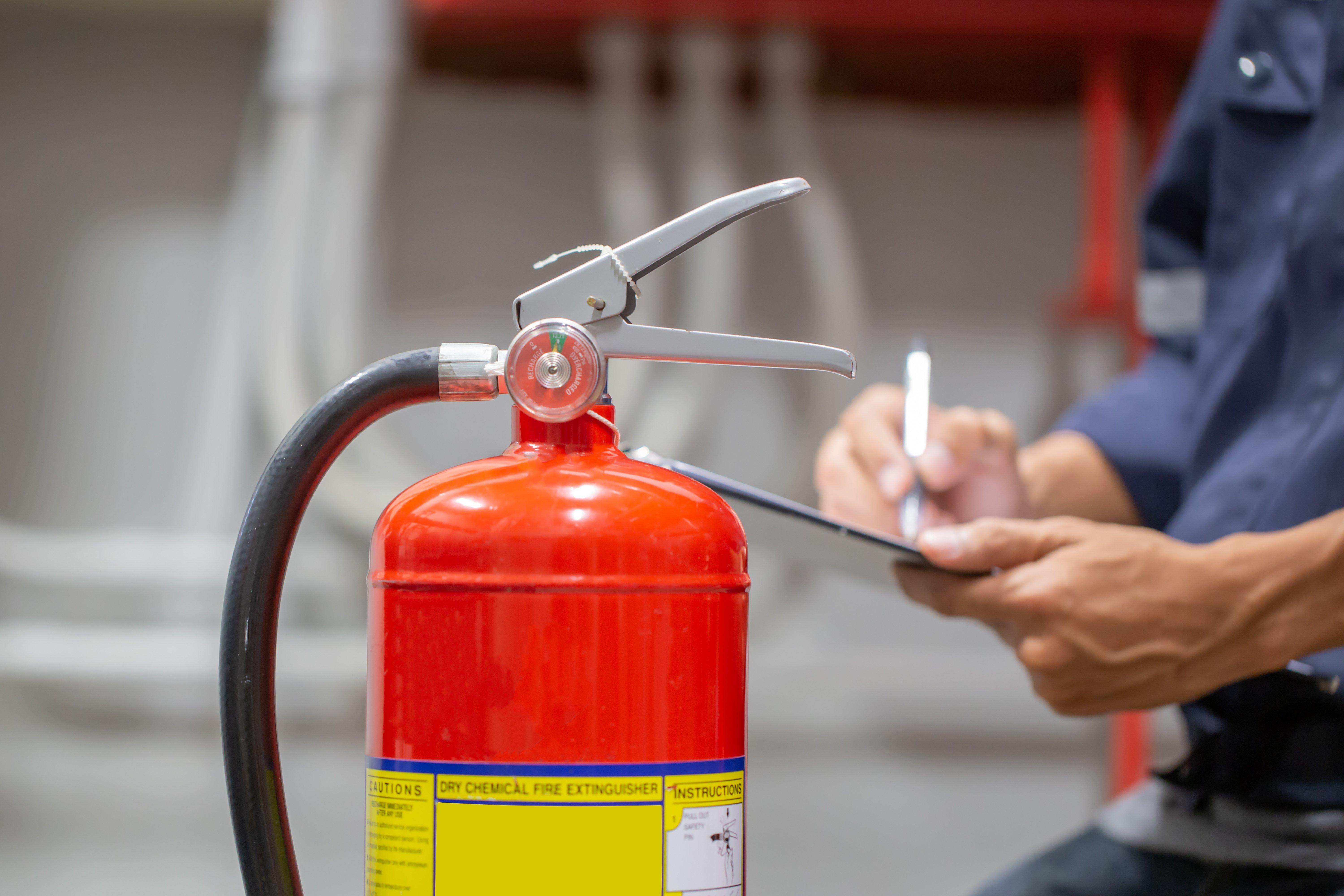 An engineer checks a fire extinguisher and writes on a clipboard in a fire control room.