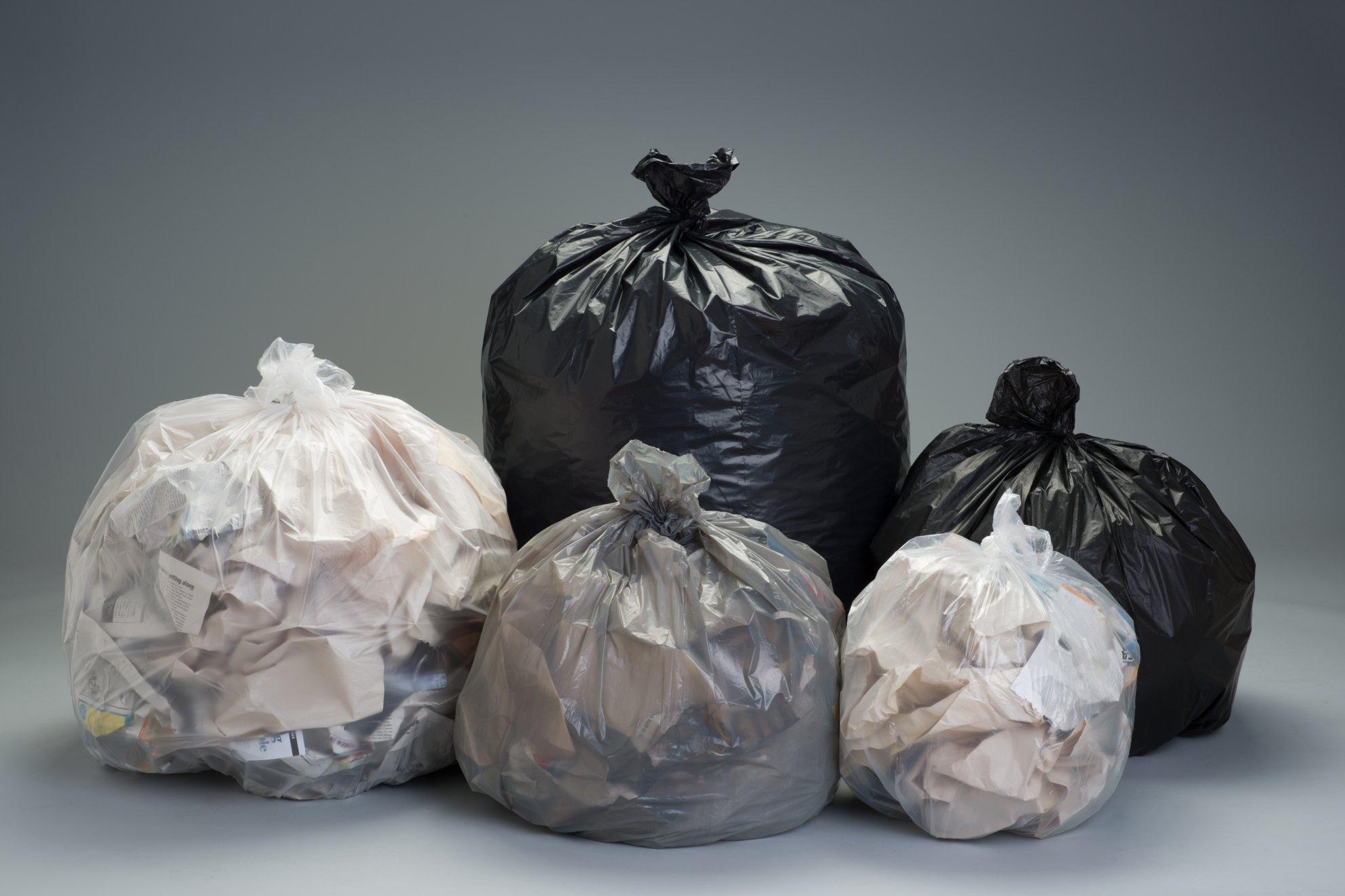 Five different-colored trash bags full of paper waste are gathered against a gray background.