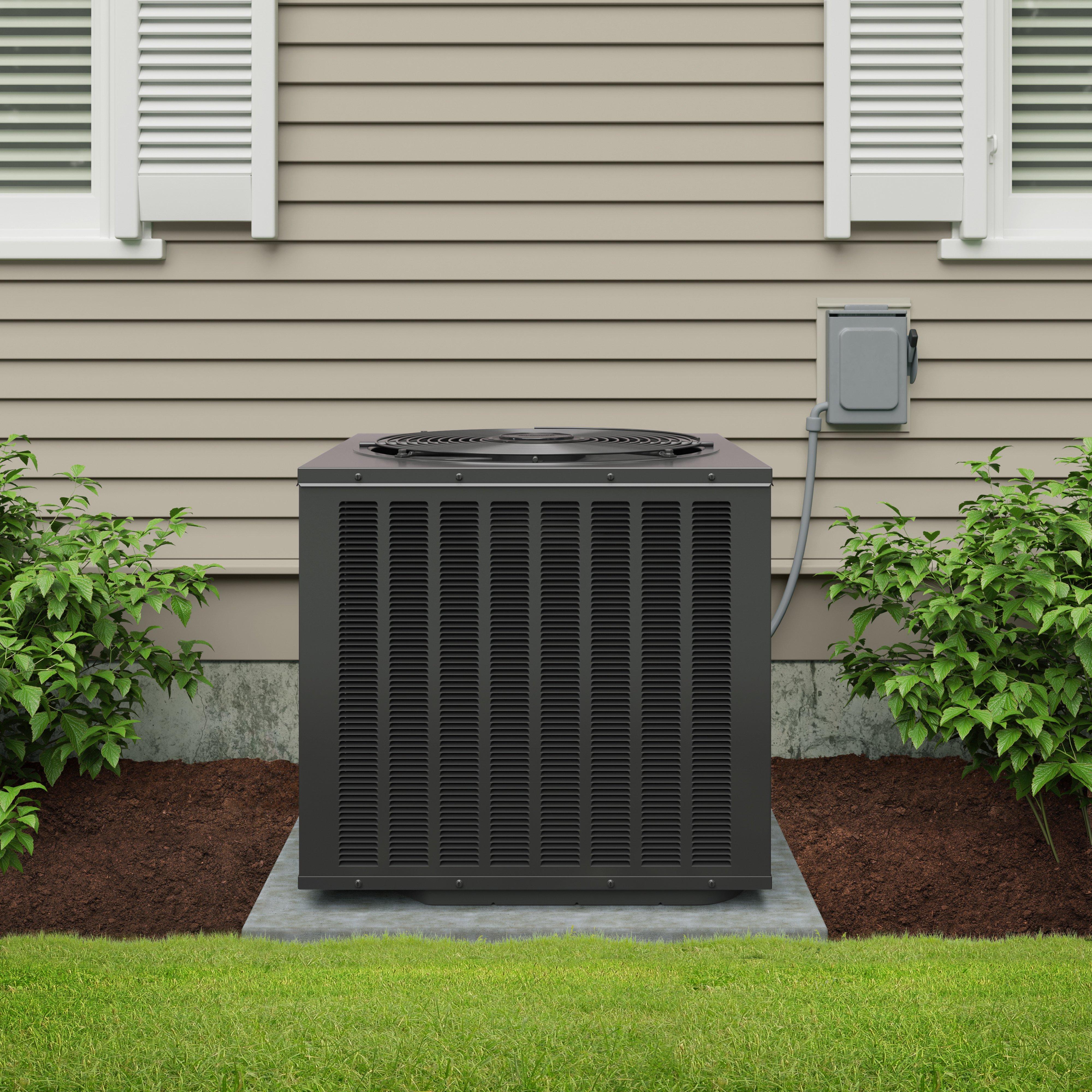 A black Durastar air conditioner condenser on a concrete pad outside of a home with beige siding and white shutters.