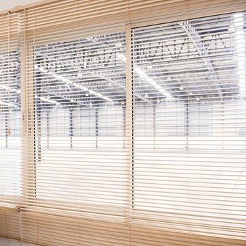 View into a warehouse from an office through open 1-inch white PVC mini blinds.