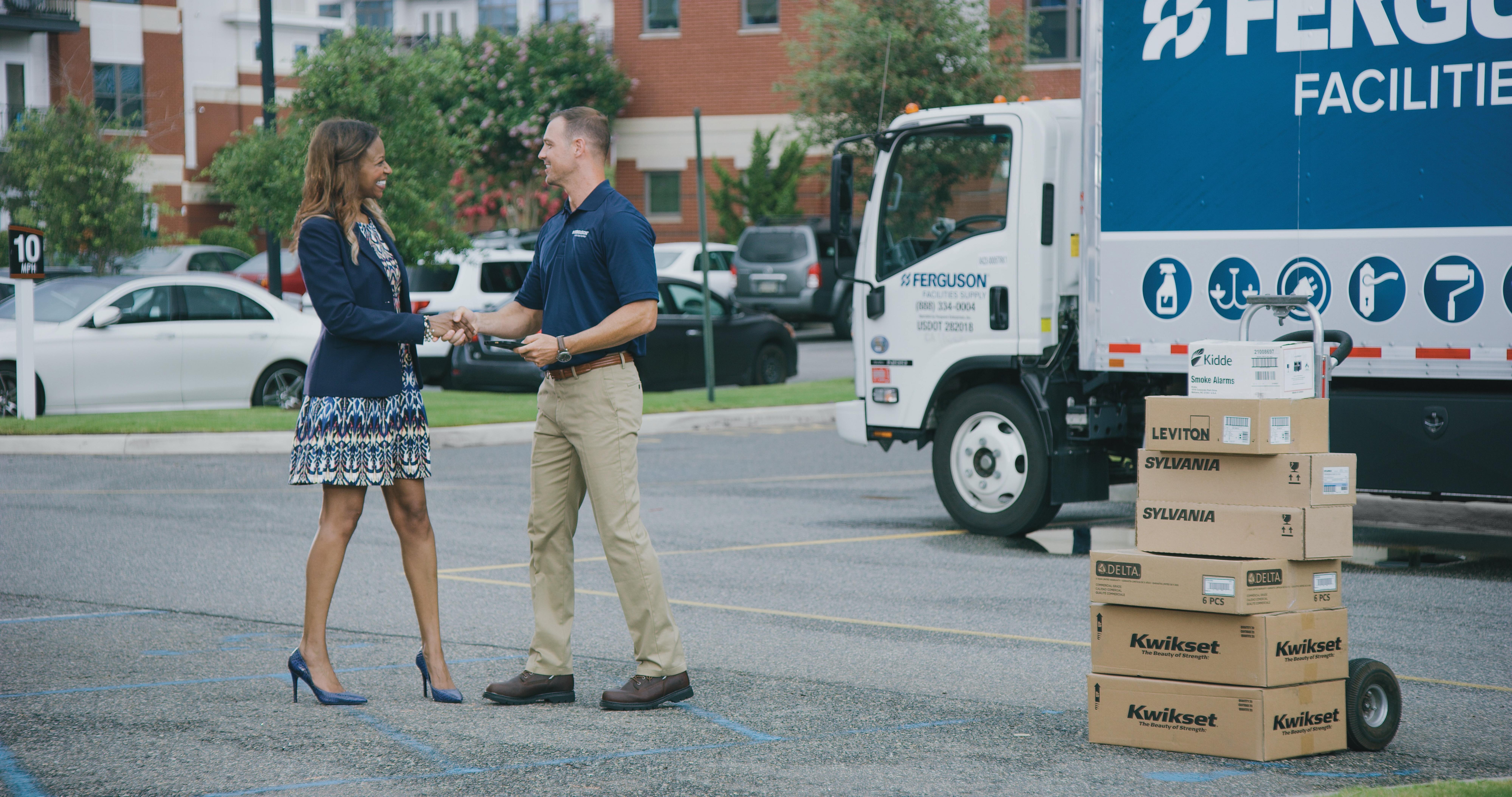 A Ferguson associate shakes hands with a customer in front of a parked delivery truck and several stacked boxes of products.