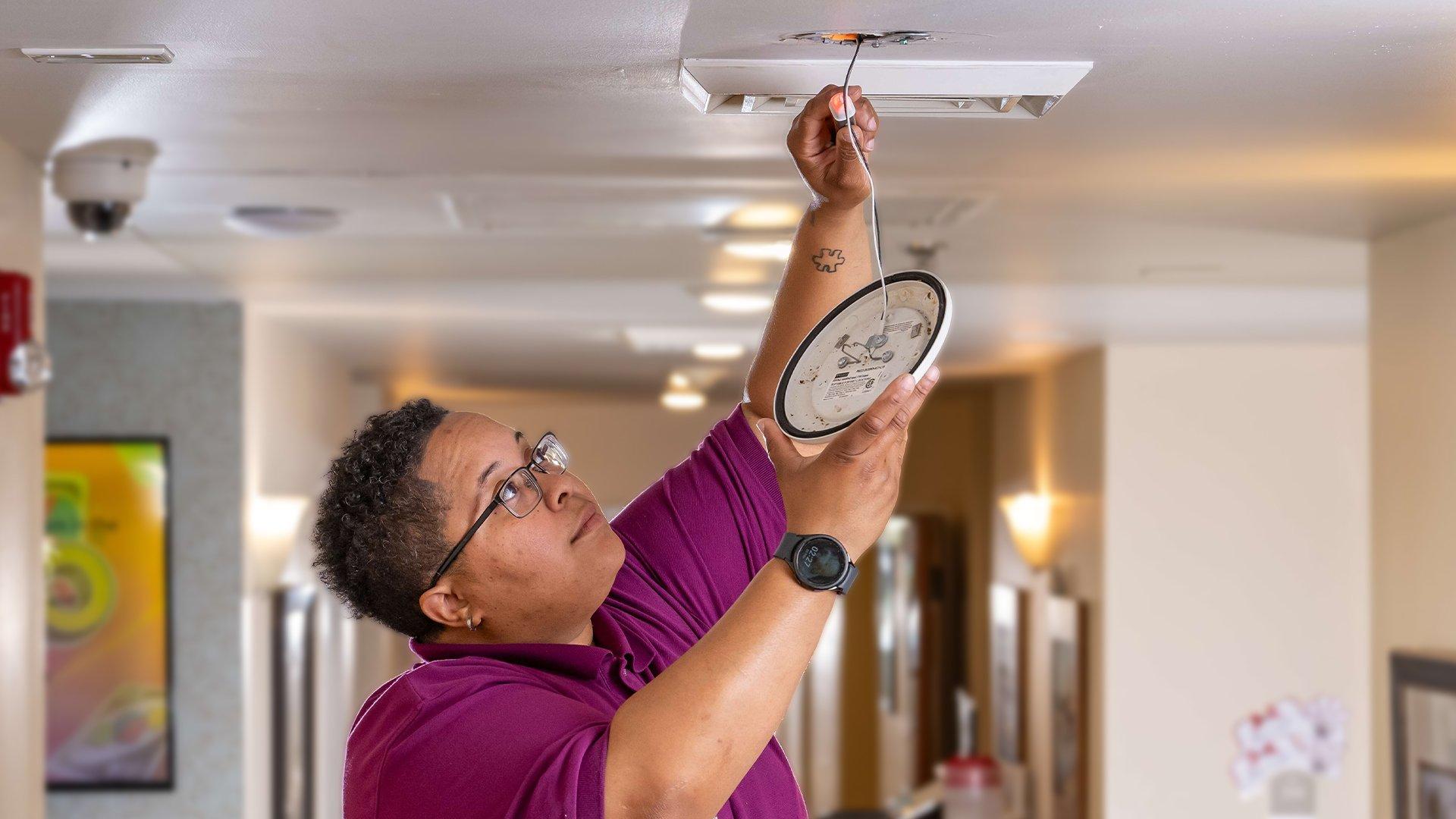 A facility manager changes a smoke alarm in a senior living facility.