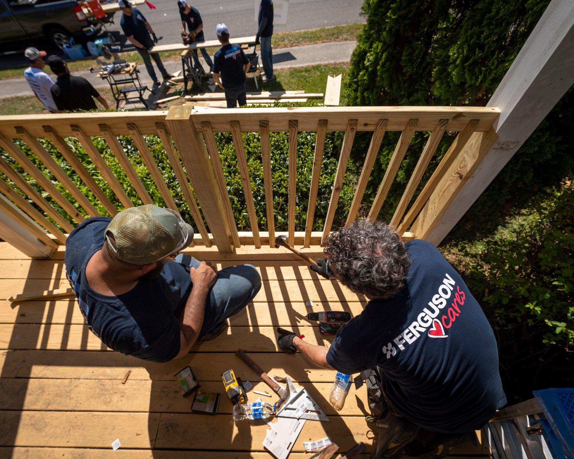 Two associates wearing Ferguson Cares T-shirts work on a wooden balcony on a residential home.