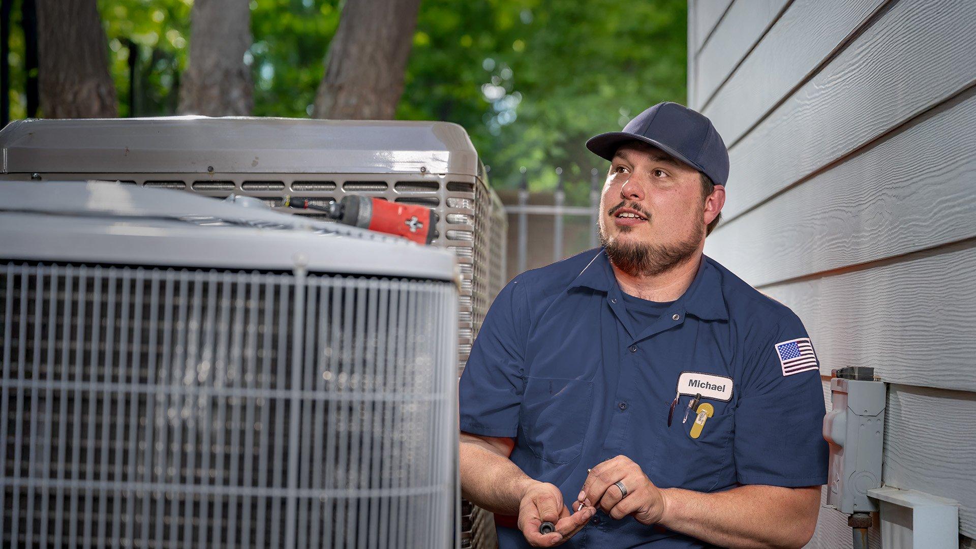 HVAC tech working on outdoor unit at residential property. 