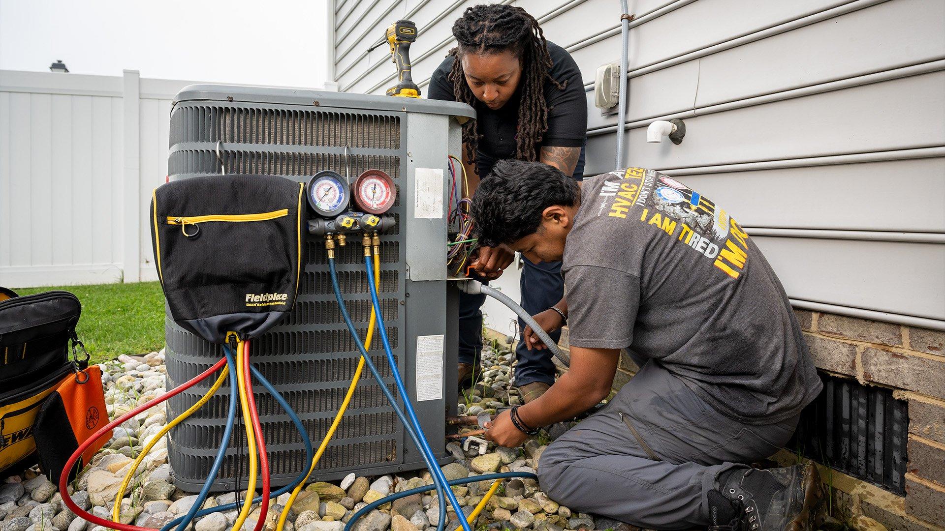 Two HVAC technicians work on outdoor unit on residential property. 
