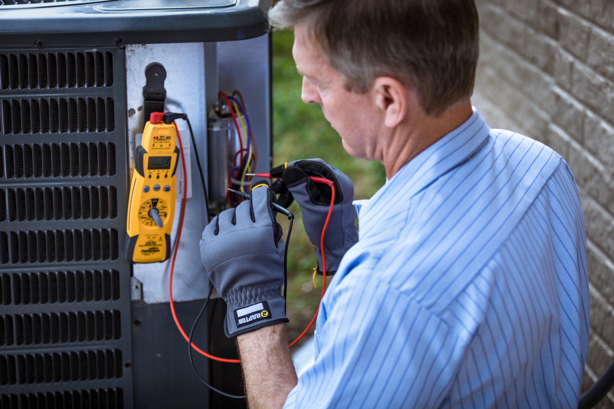 An HVAC technician checks voltage on a residential air conditioner condenser.