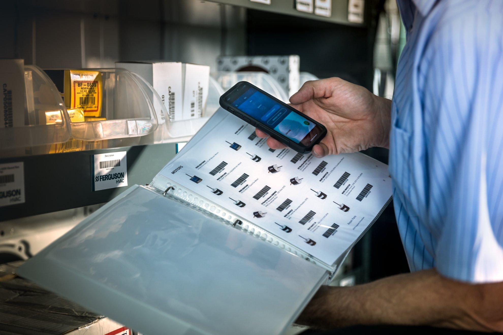 An HVAC technician uses his phone to scan barcodes of parts in a price book.