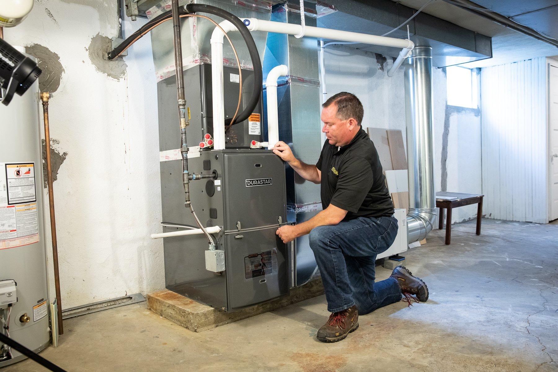 A man kneeling next to an HVAC system in a basement.