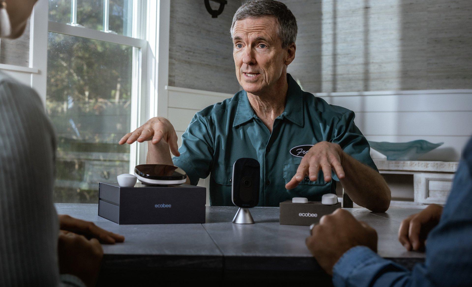 An HVAC contractor sits at a kitchen table and discusses an ecobee smart thermostat with homeowners.