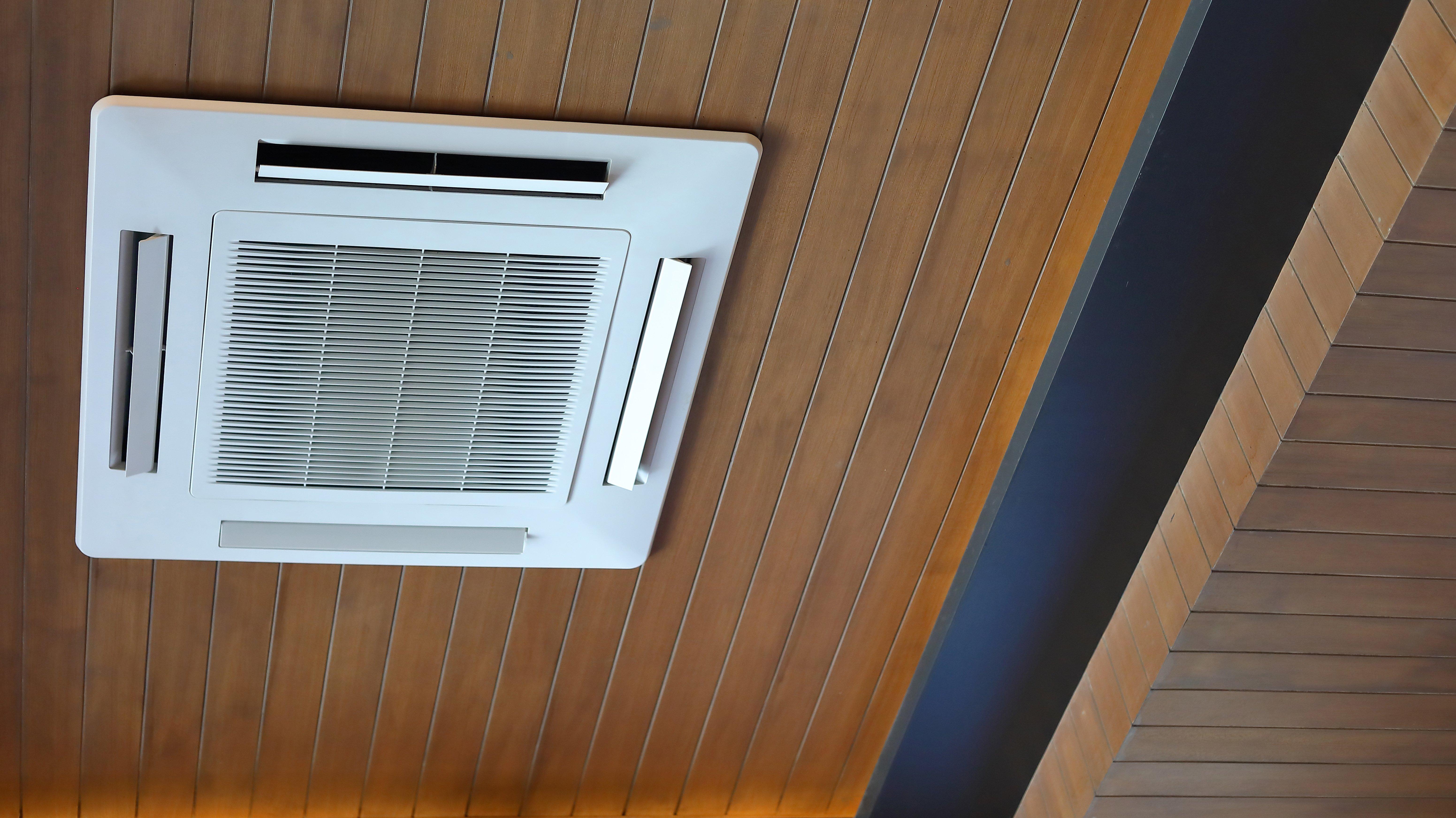 A mini-split air conditioner cooling cassette is installed on a wooden ceiling.