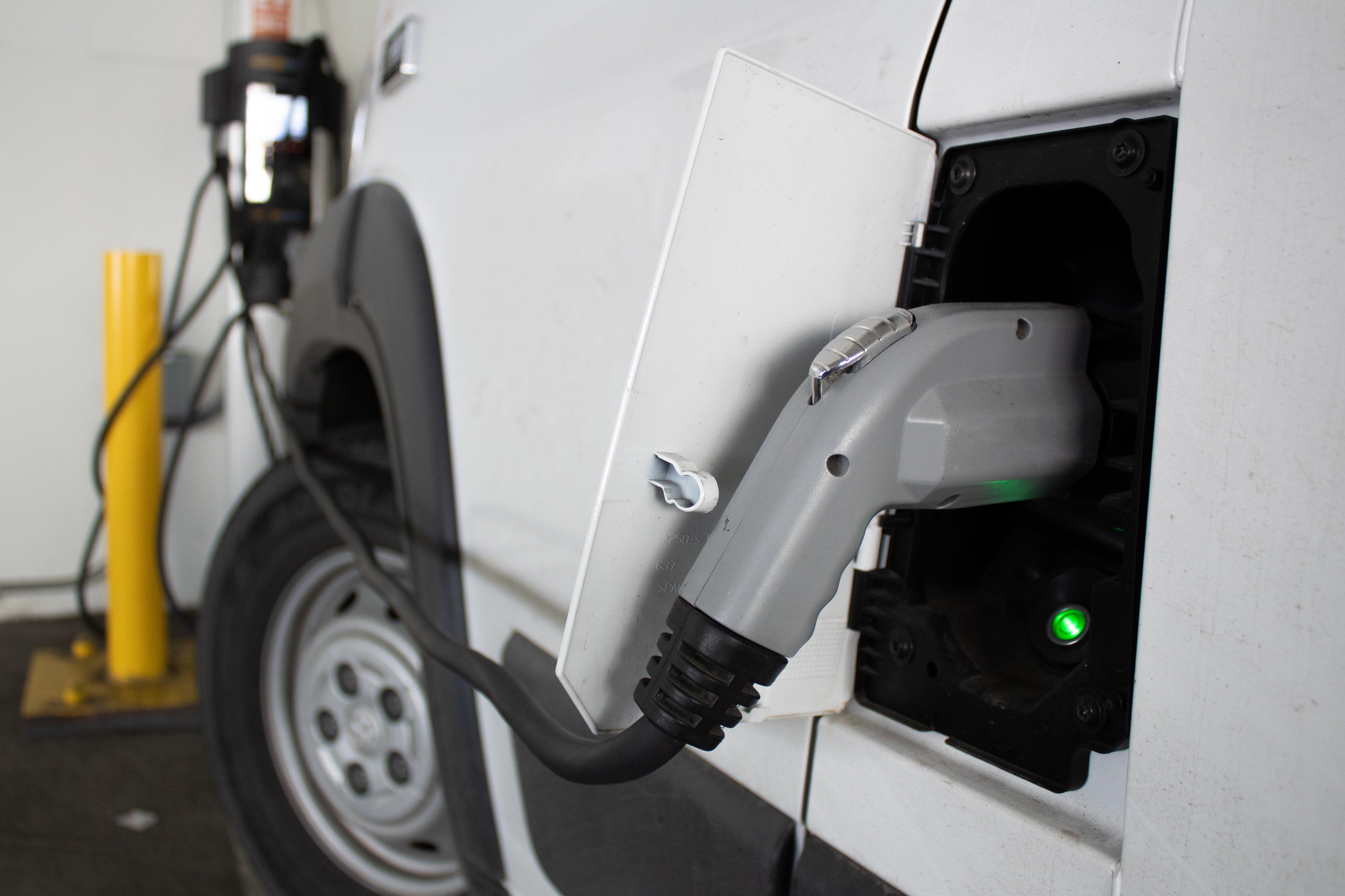 A white car is plugged into a public electric vehicle charging station.