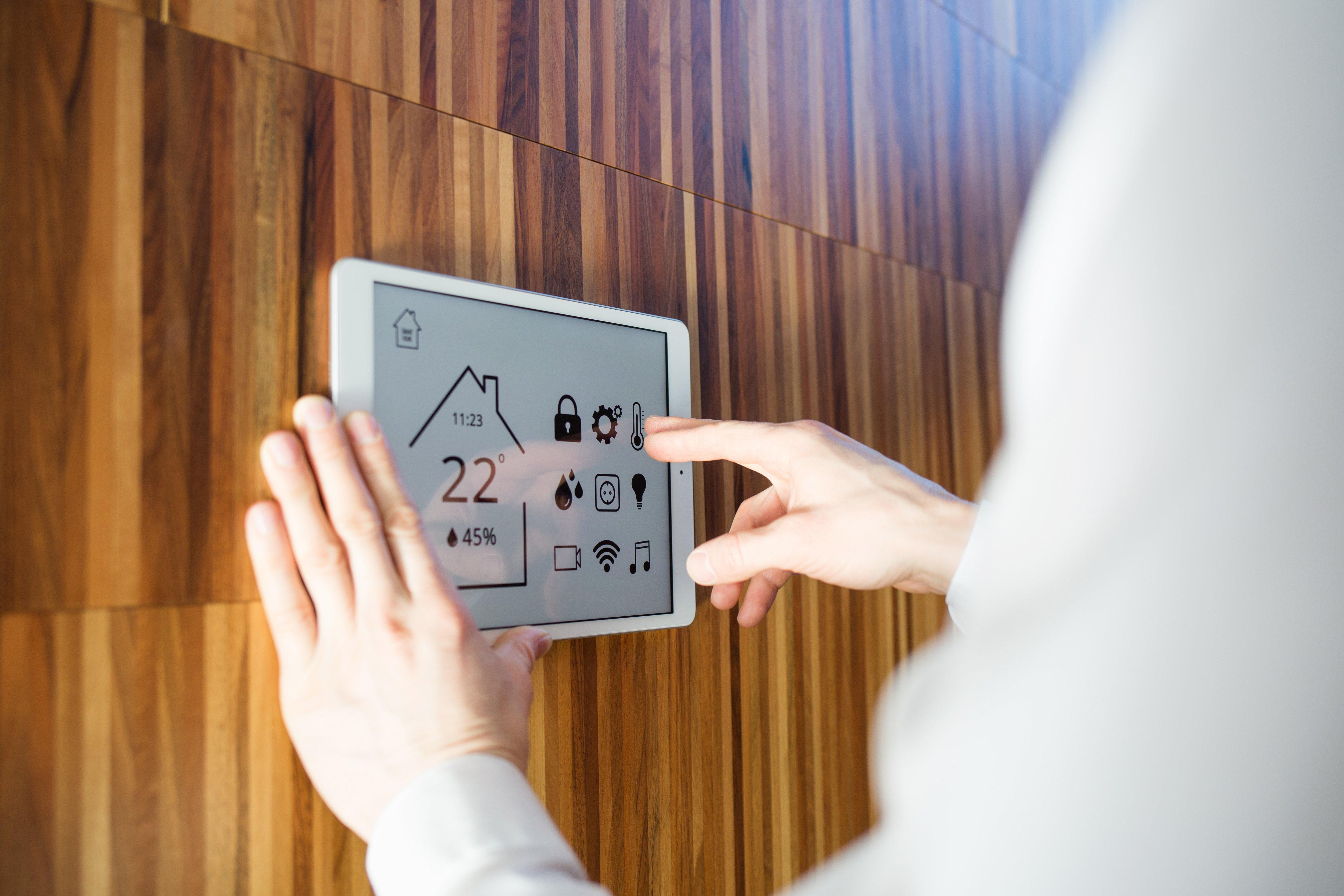 A man controls smart home devices using a digital tablet against a wooden wall.