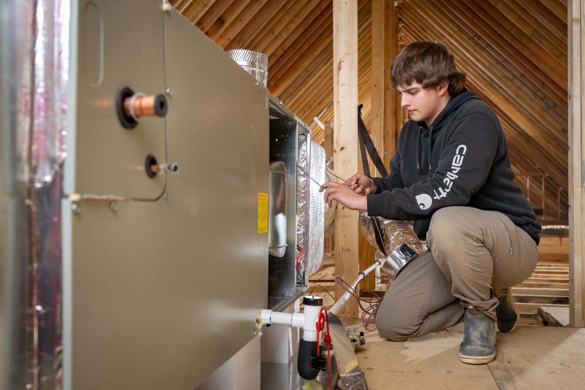 An HVAC technician performs duct work on the distributor in a residential attic.