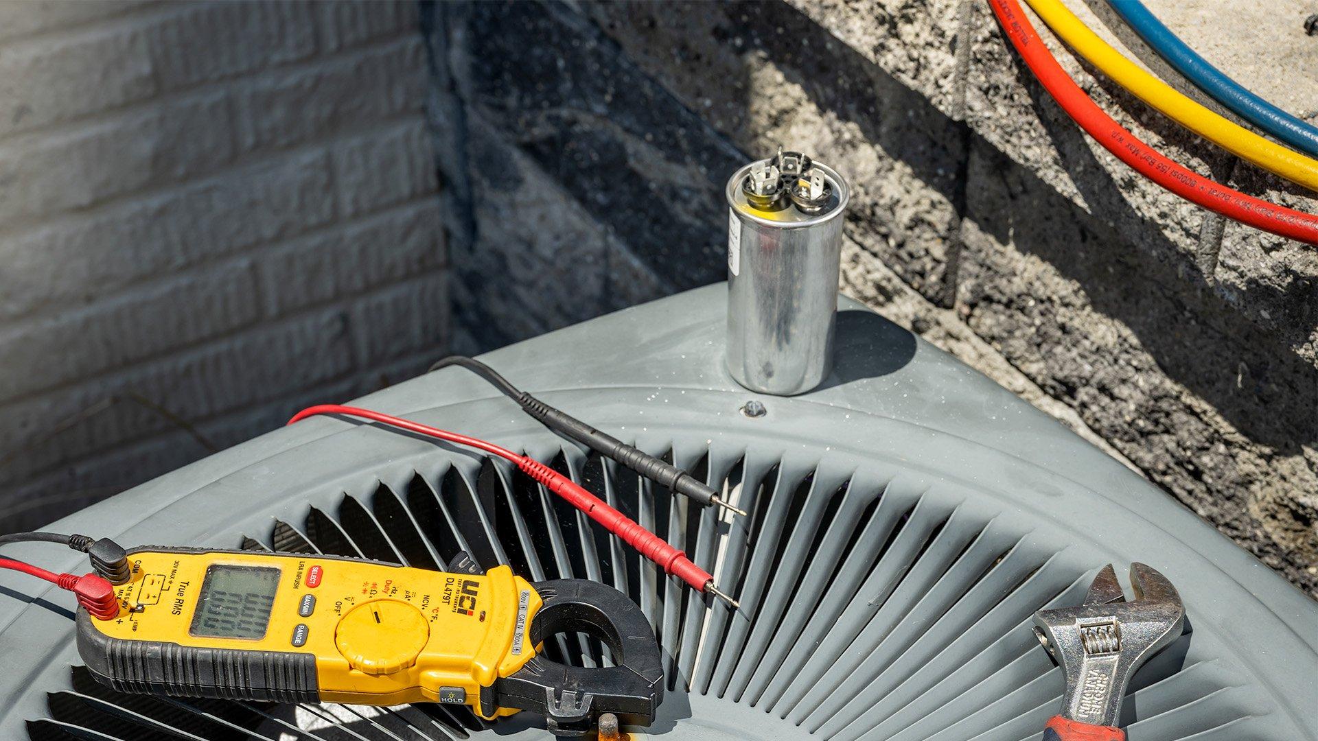Capacitor, multimeter and wrench sit on top of HVAC condenser unit.
