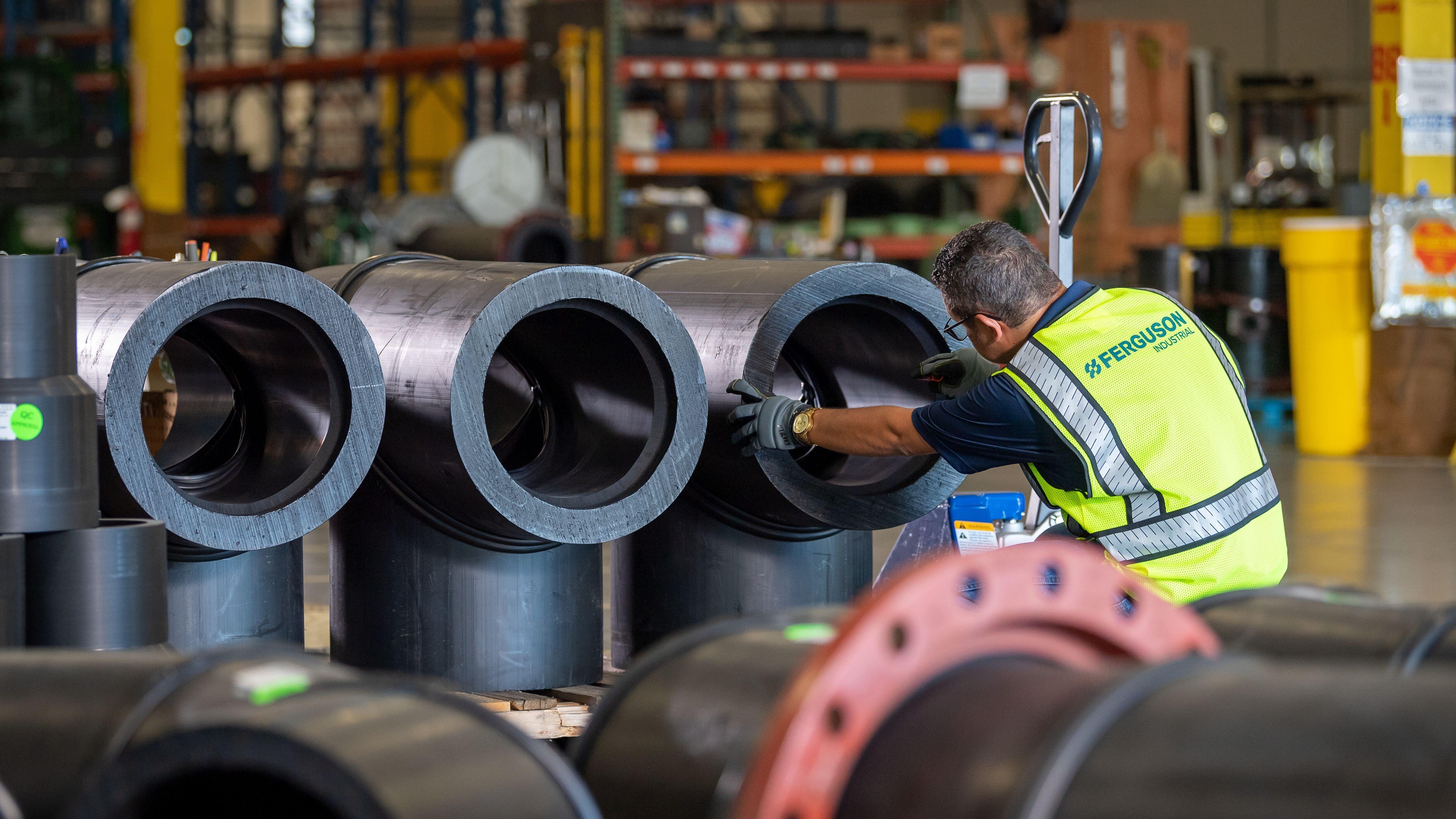 Ferguson associate arranges large, black, T-shaped pipe fittings on a pallet in warehouse. 