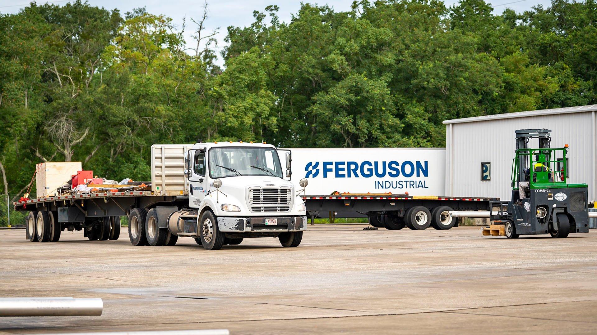 Flat-bed semi truck on a work site with a semi trailer and construction equipment in the background.