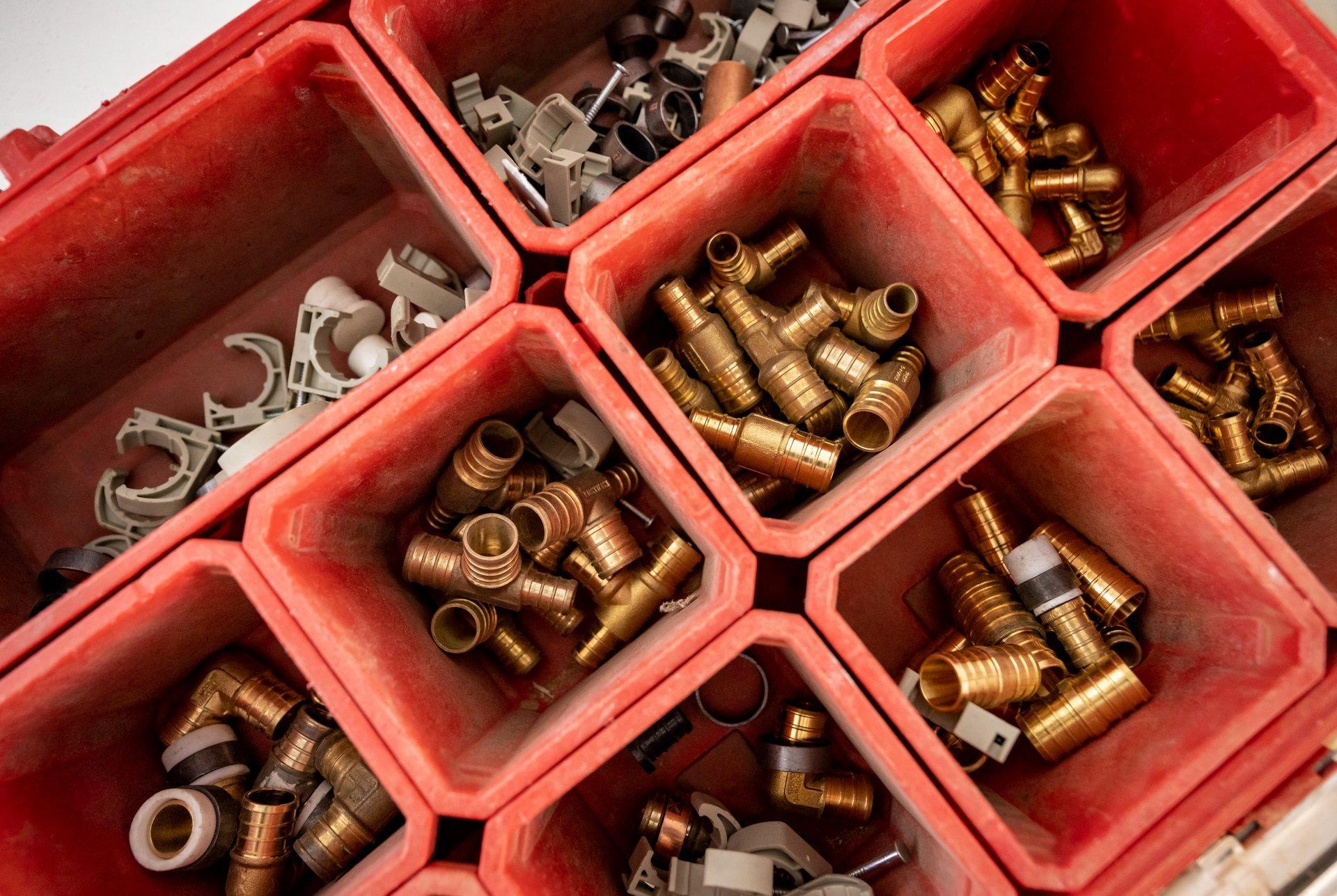 View from above of brass and copper pipe fittings and parts separated into red containers.