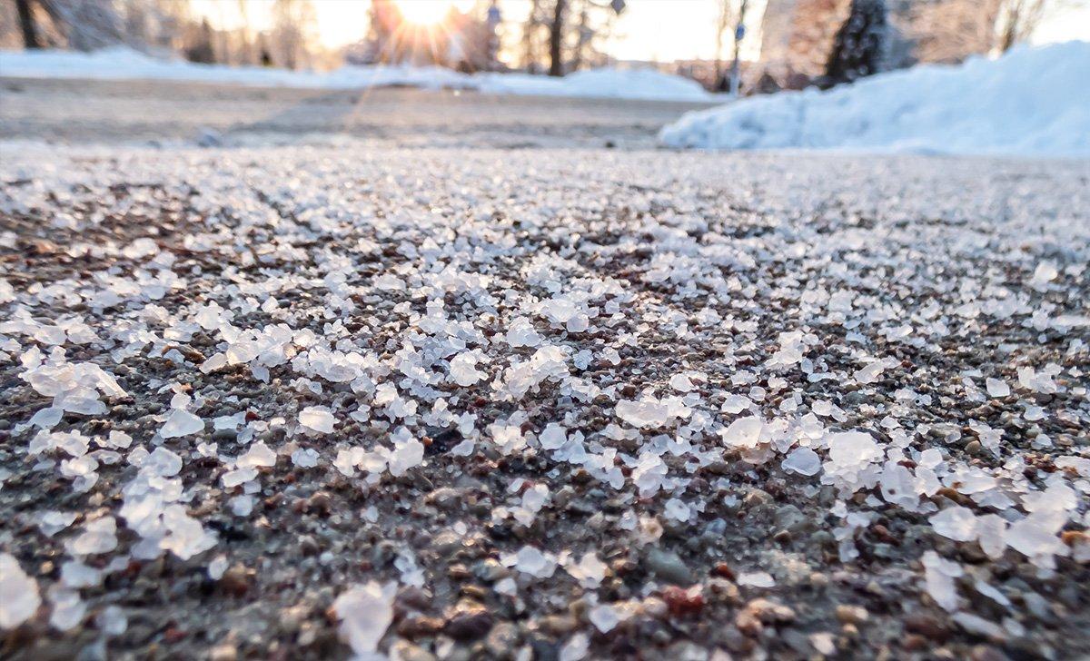 Salt grains on icy sidewalk in winter