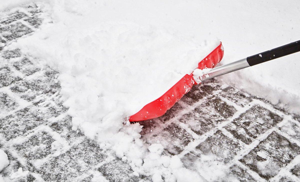 Red snow shovel pushing snow on a brick walkway