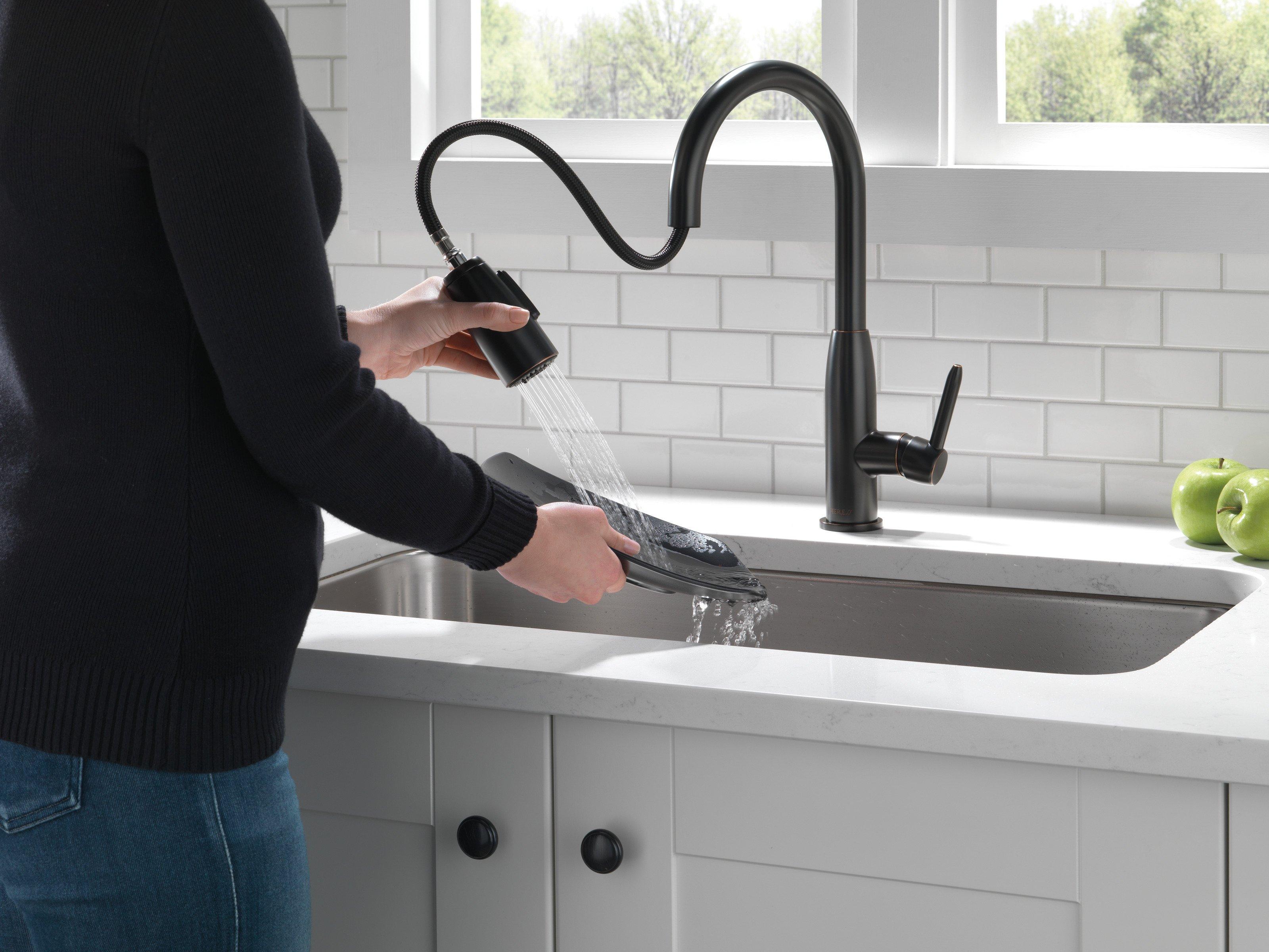 A woman uses a black pull-down kitchen faucet to rinse a plate in her home.