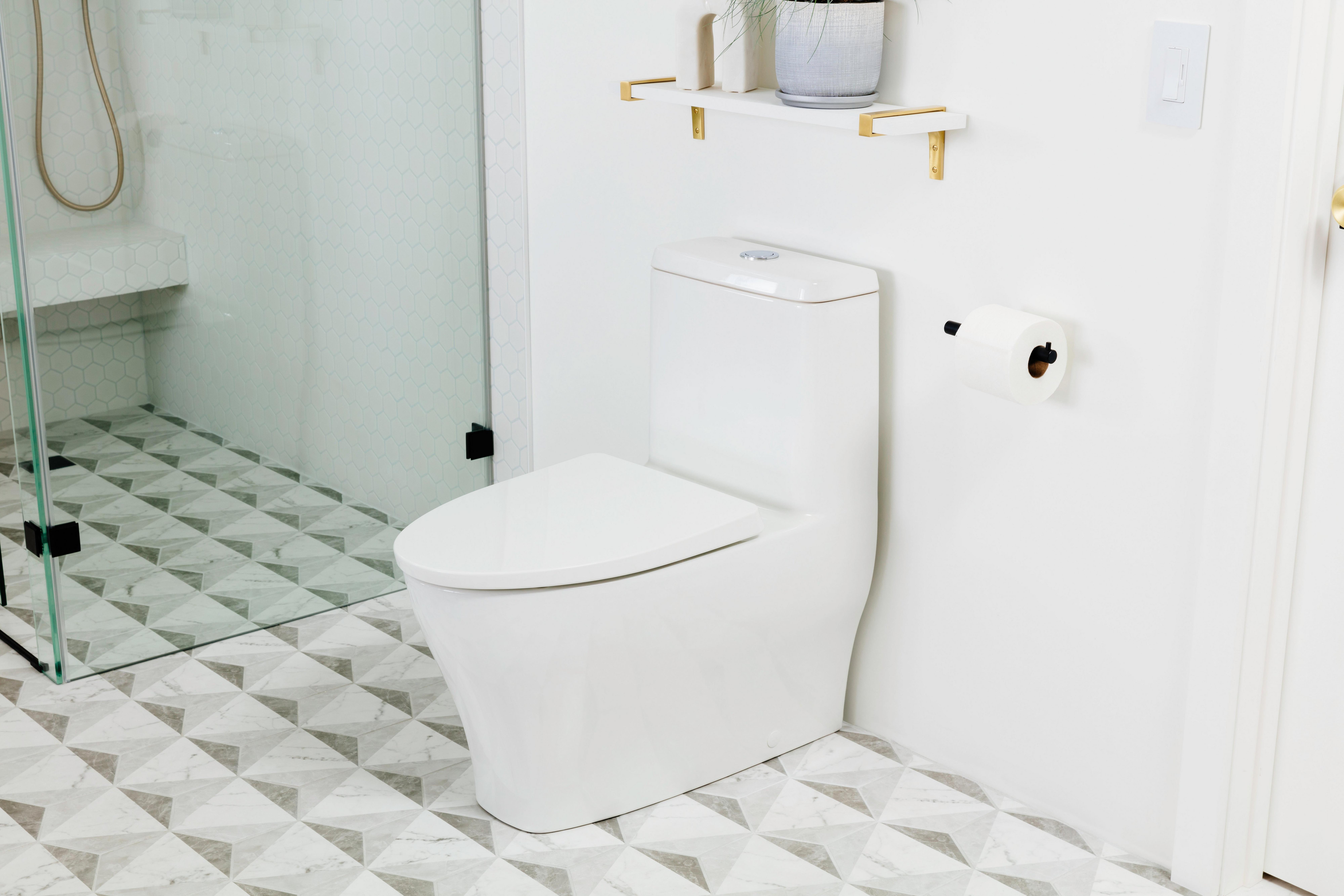 A white one-piece elongated toilet is installed next to a glass shower in a residential bathroom.