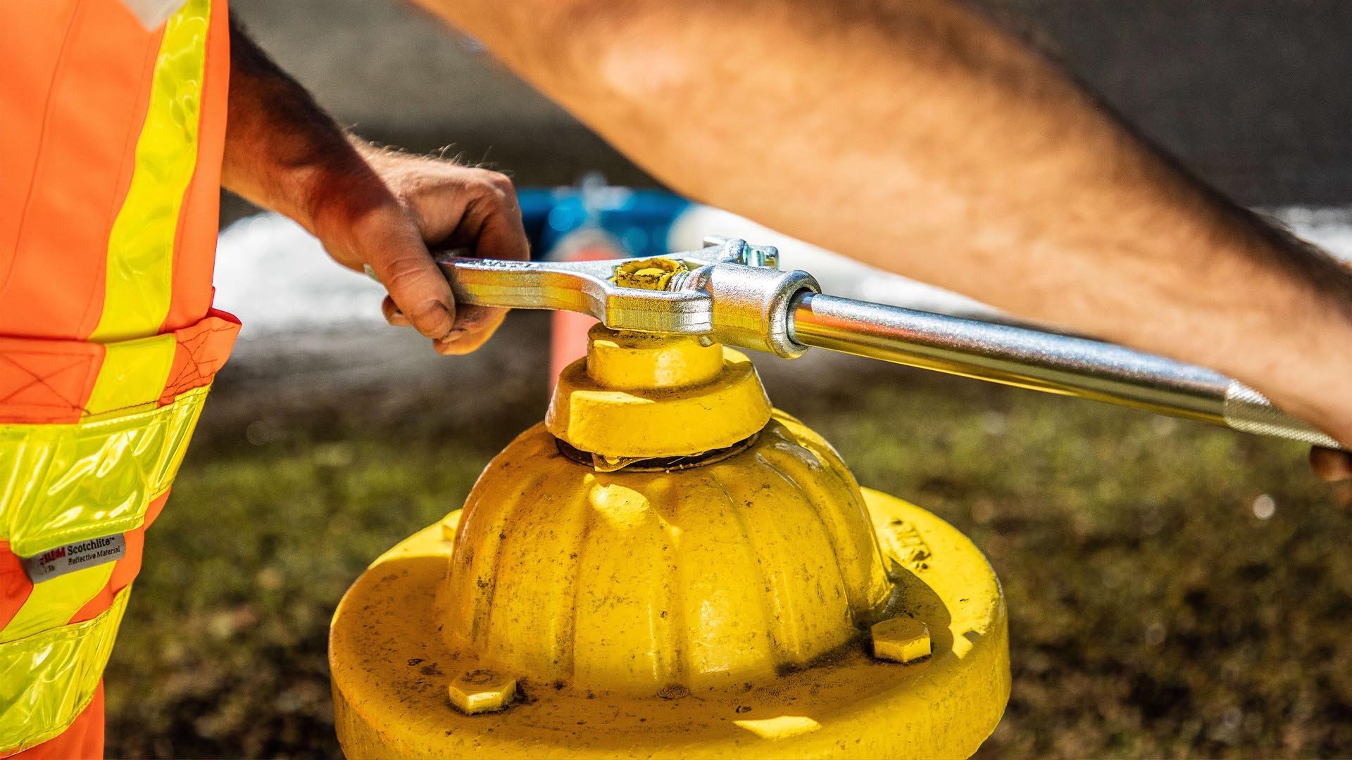 Worker in safety vest uses tool to open yellow fire hydrant.