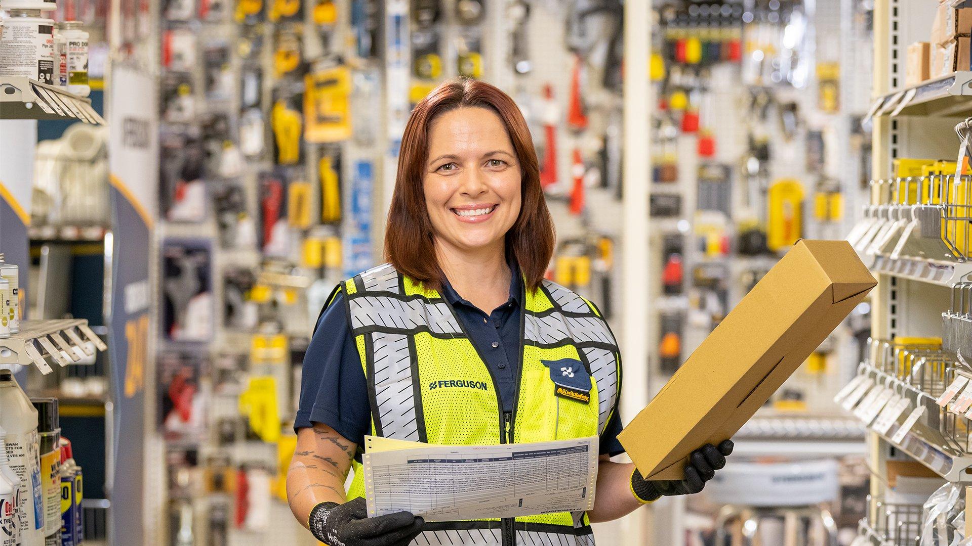 A smiling Ferguson associate stocks products in an aisle at a counter location.