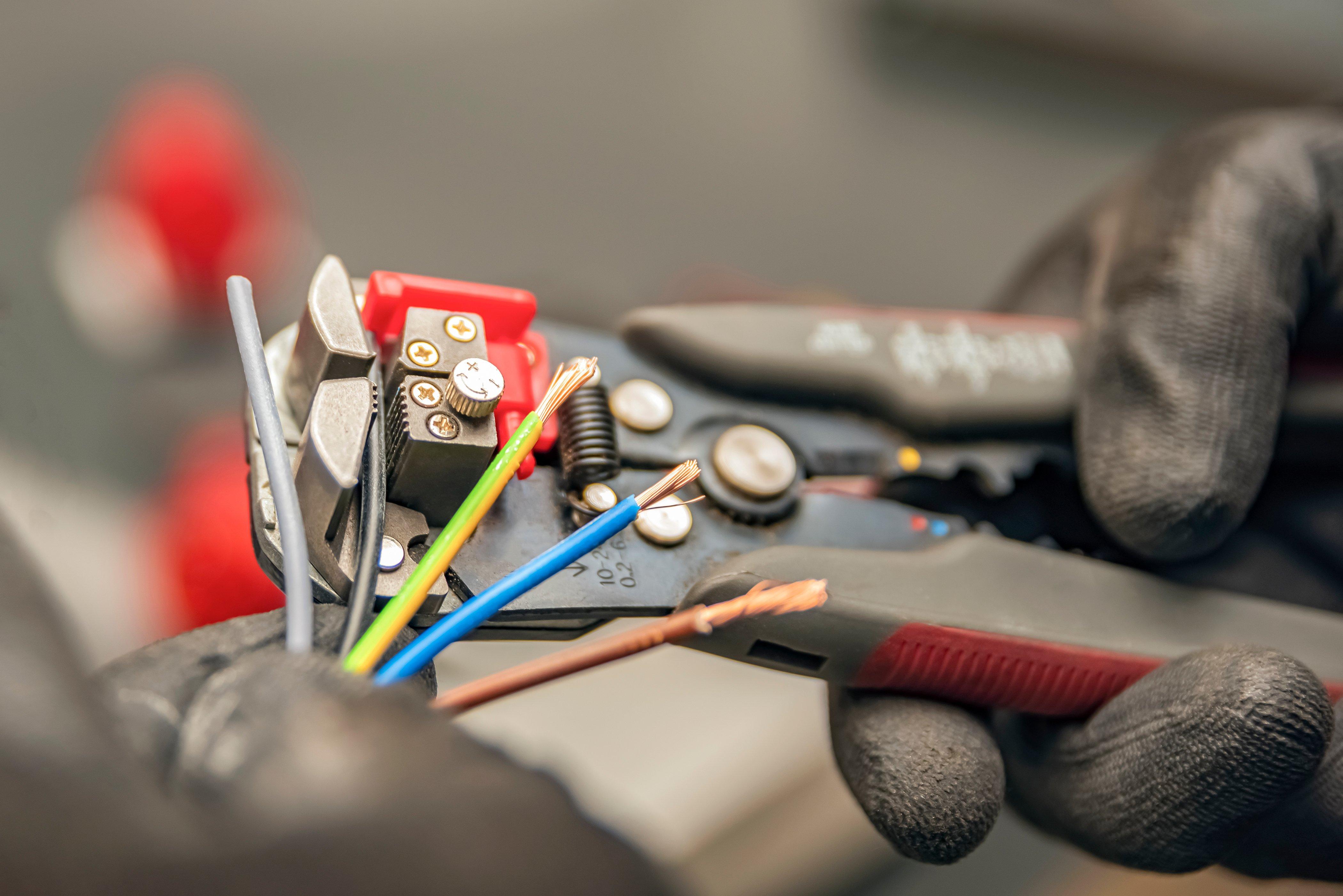 Gloved hands use a wire stripper to clean the protective insulation from a wire.