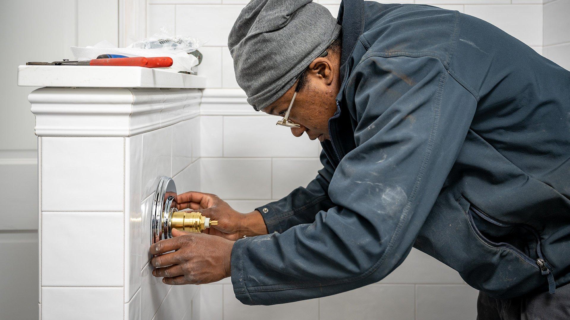 Plumber installing a new shower valve in a white tile shower