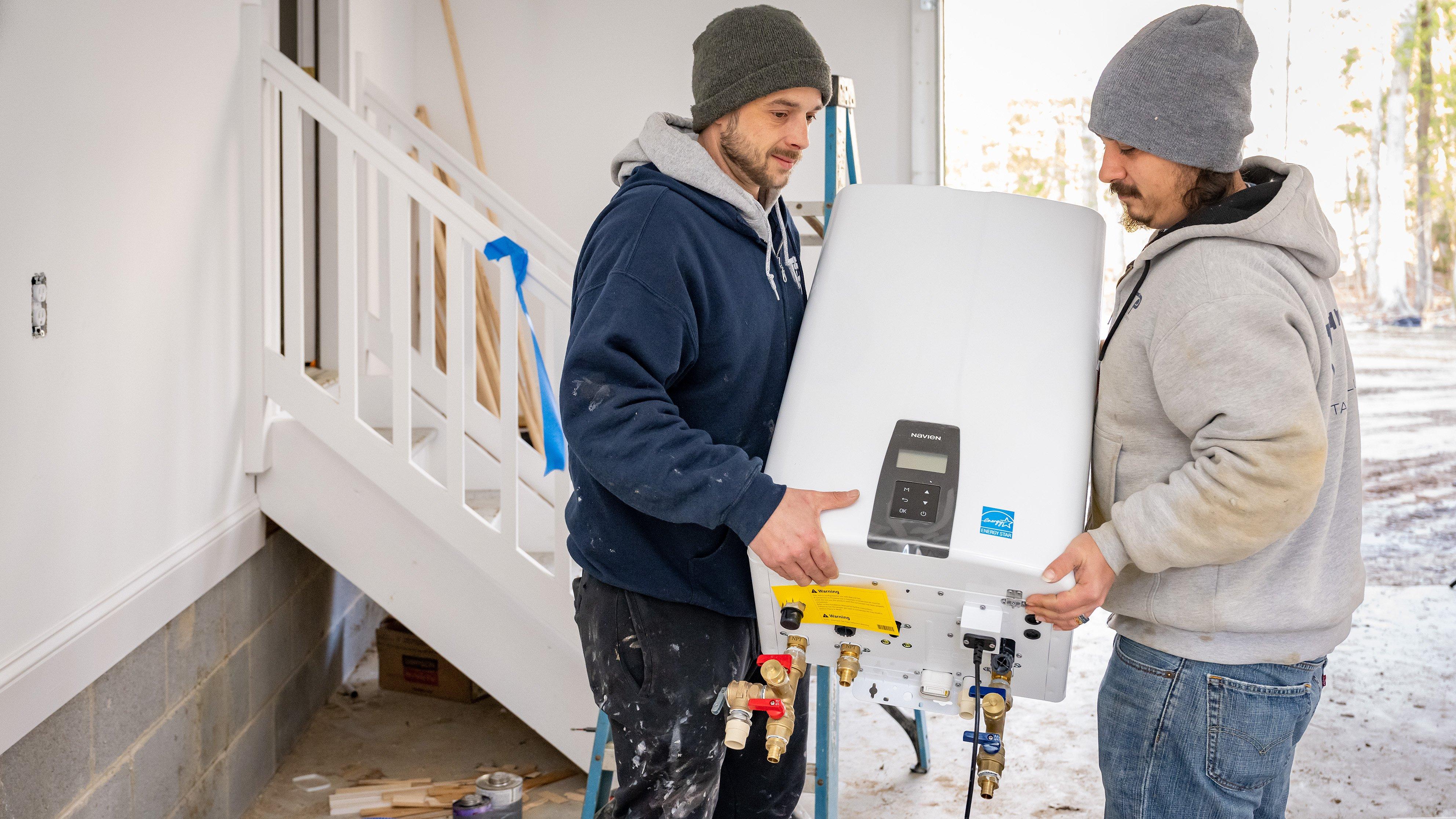 Two contractors carry an EnergyStar water heater in a home’s garage.