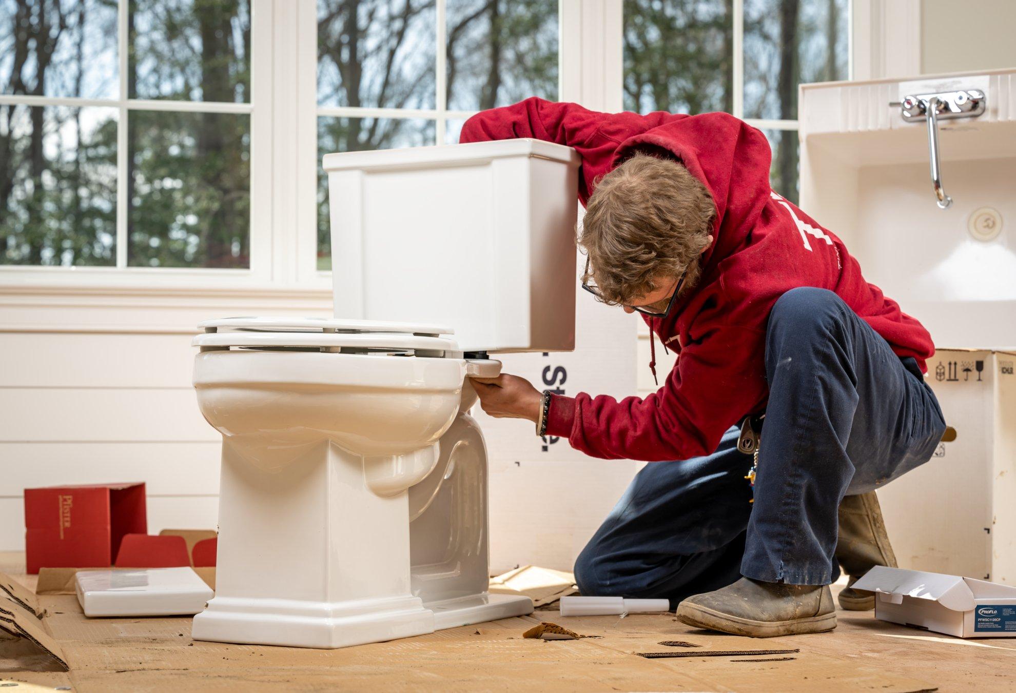 A contractor assembles a new toilet in a residential bathroom.