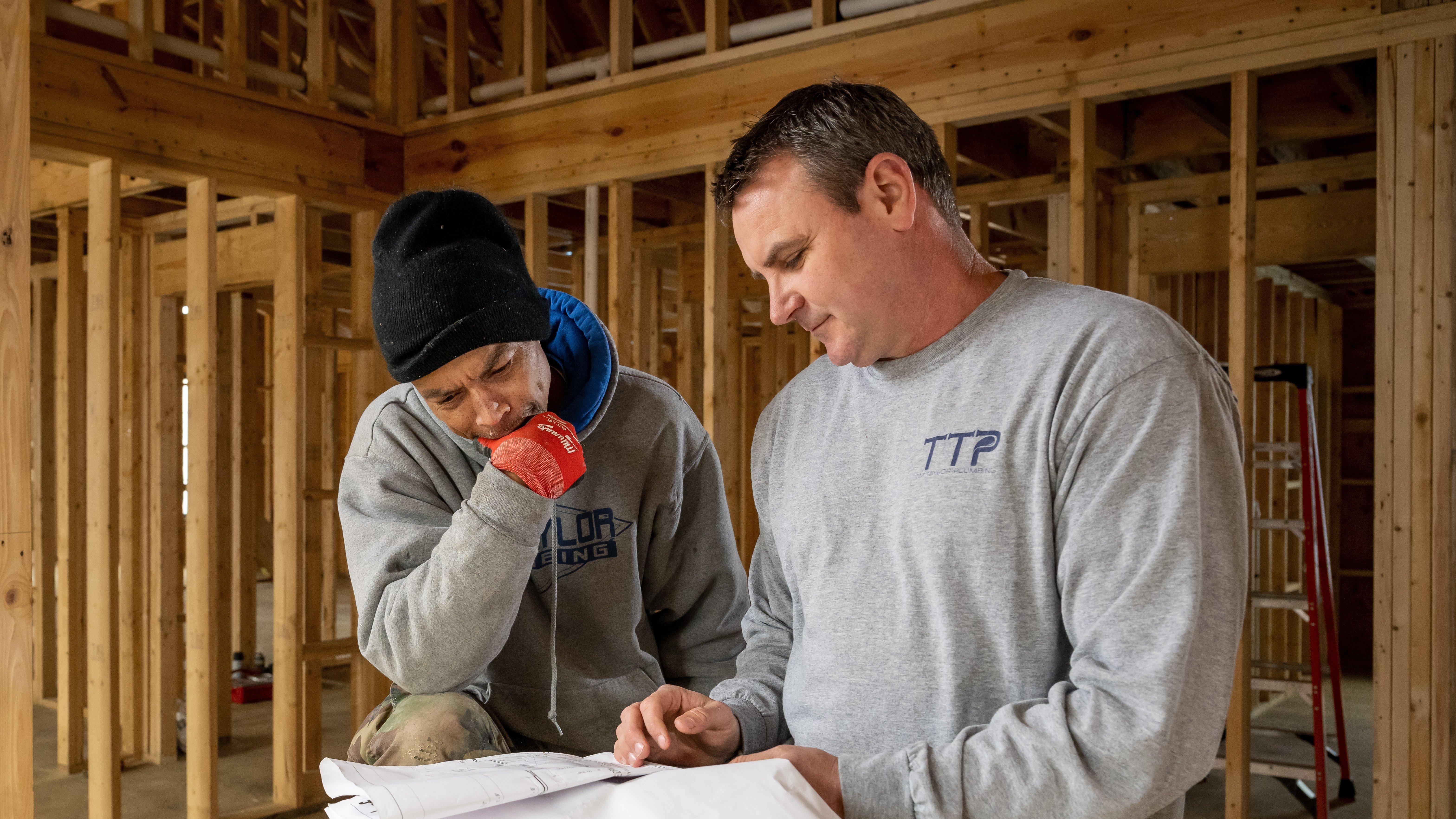 Two contractors in a residential new build review blueprints.