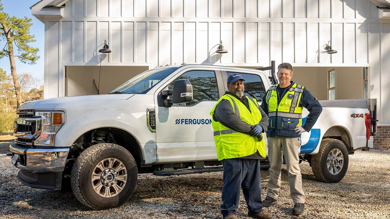 Two Ferguson associates wearing reflective gear stand in front of their work truck.