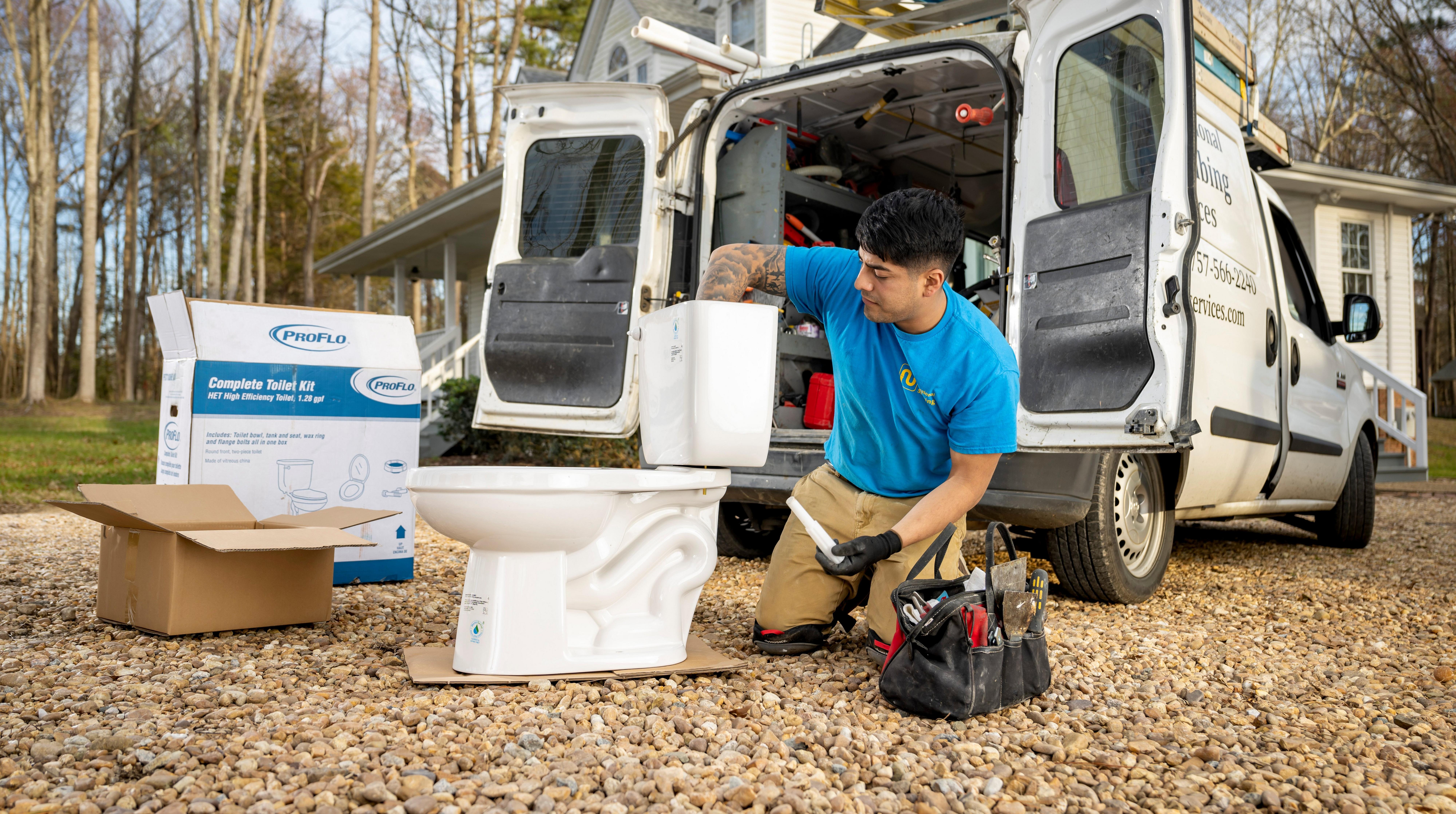 A plumber works on a toilet outside of his work van.