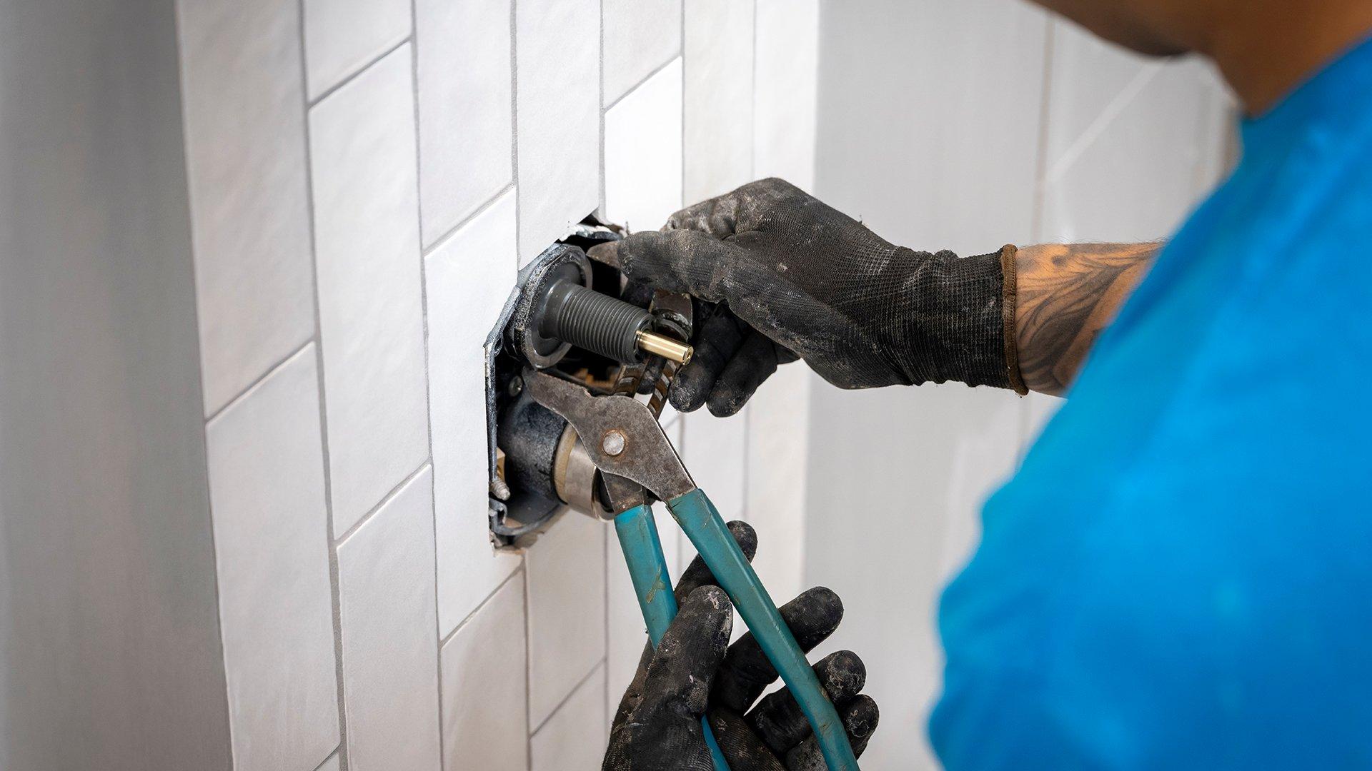 In a residential bathroom, a plumber prepares shower pipes for a new installation.