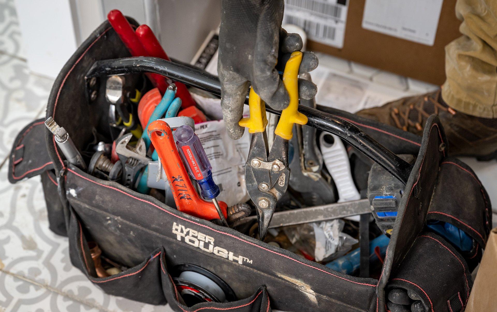 A plumber’s tool bag overflows with tools in a residential bathroom.
