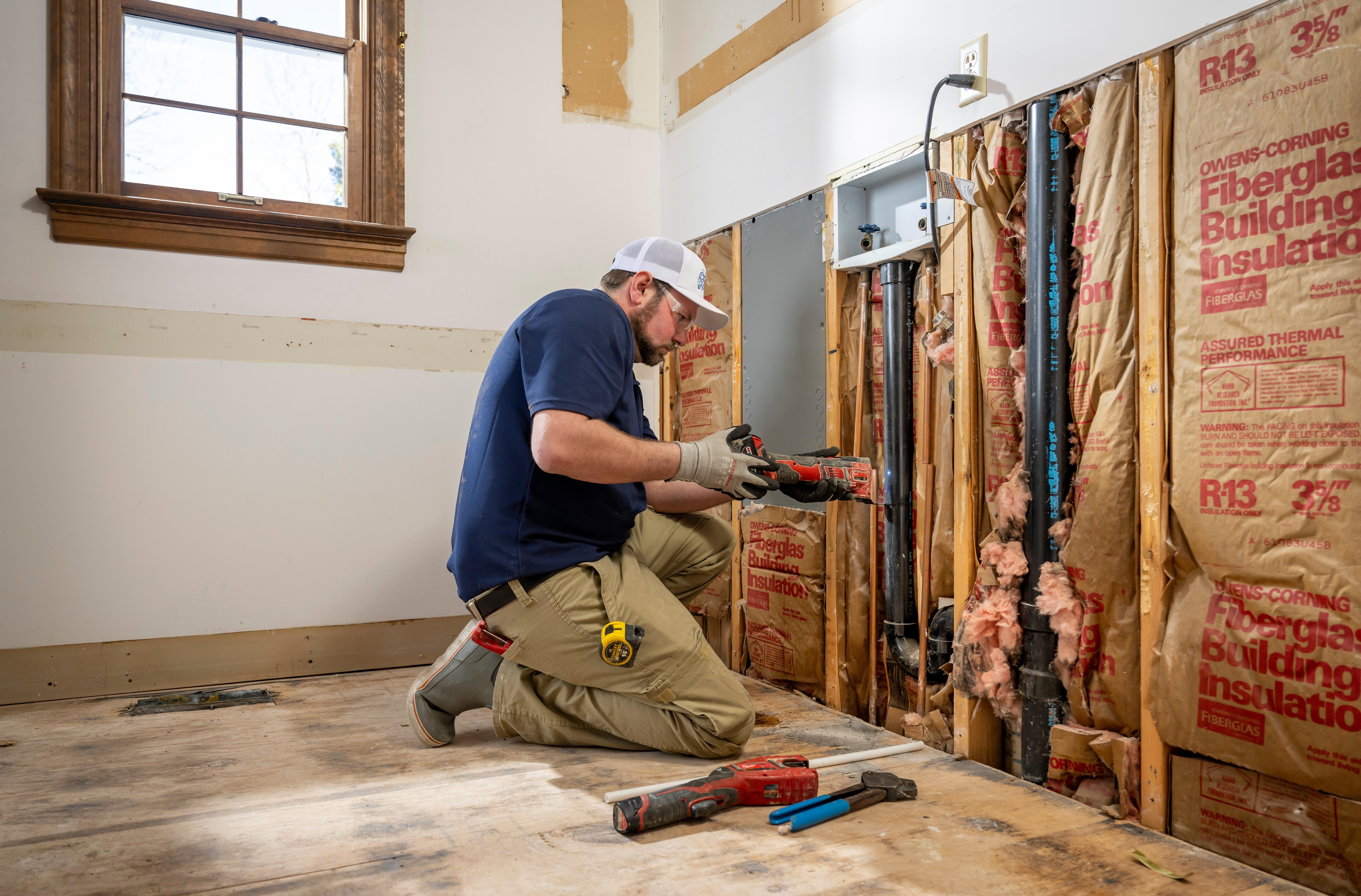 A plumber cuts PVC pipe in a laundry room in a new build.
