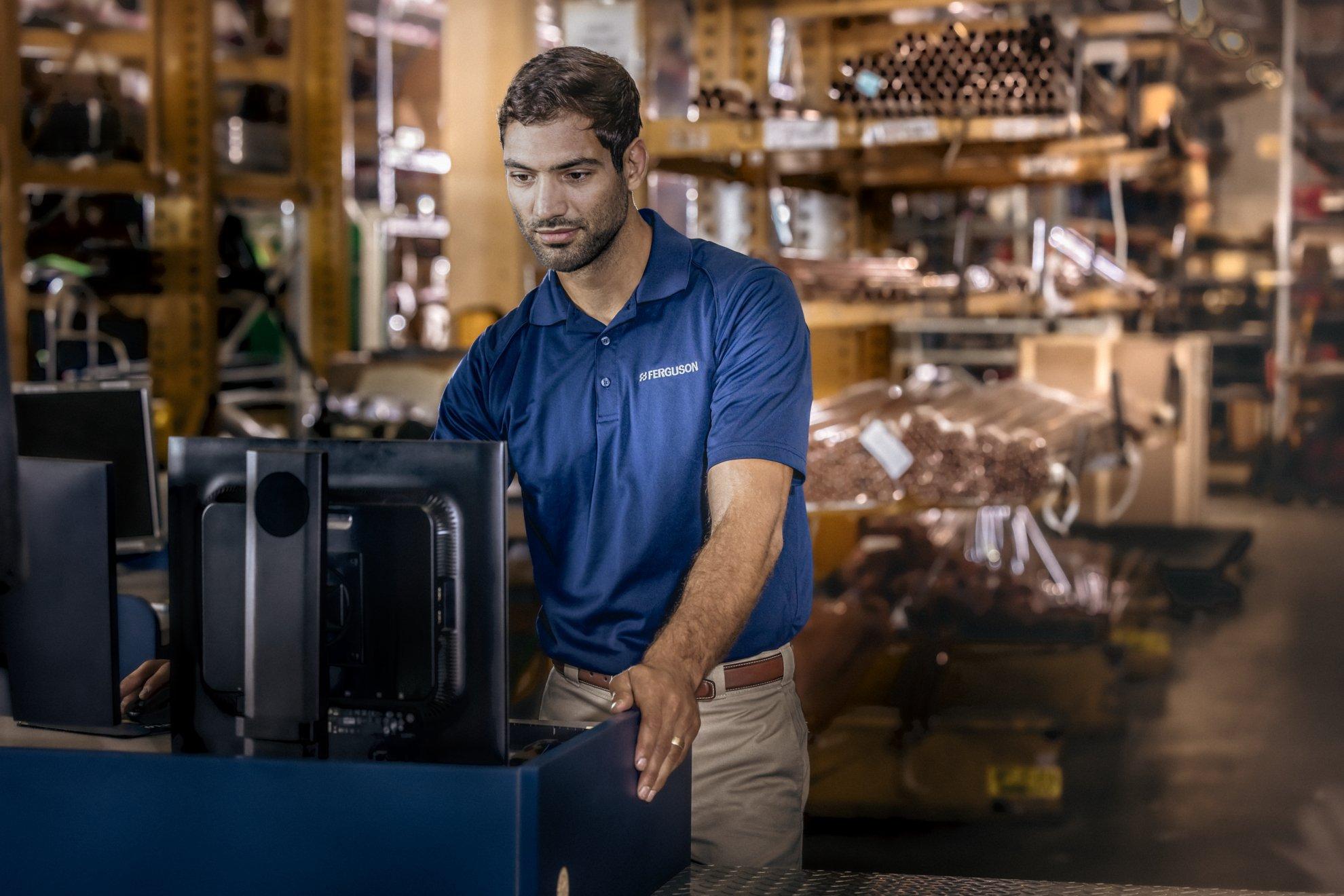An associate using computer in a warehouse with stacked copper pipe.