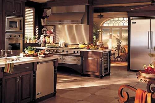 A large modern kitchen in earth tones and brass with a double oven range, a convection oven, and an island with dishwasher and sink.