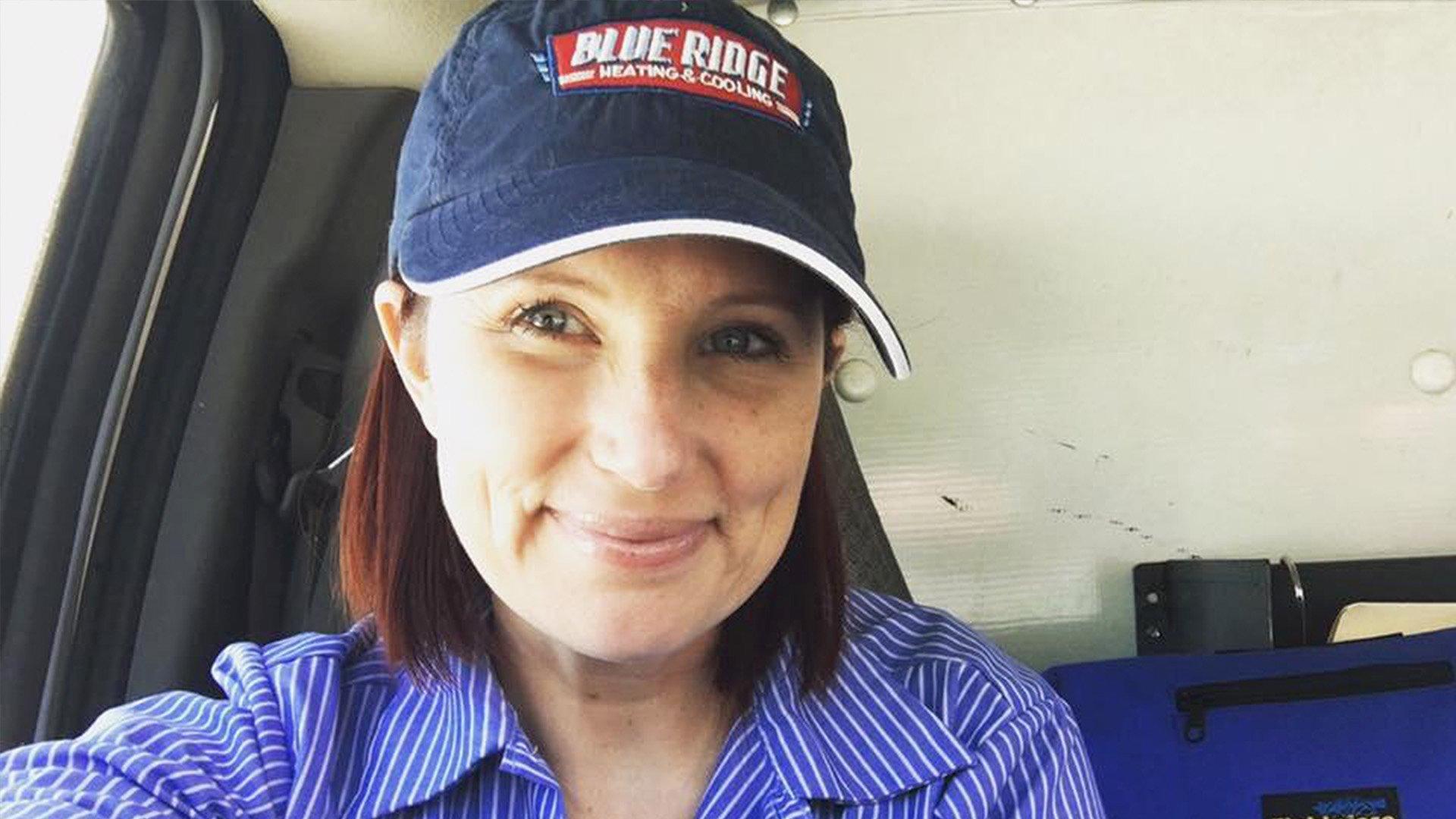 In a selfie, Jennifer S wears a Blue Ridge Heating & Cooling hat and striped shirt in her work truck.