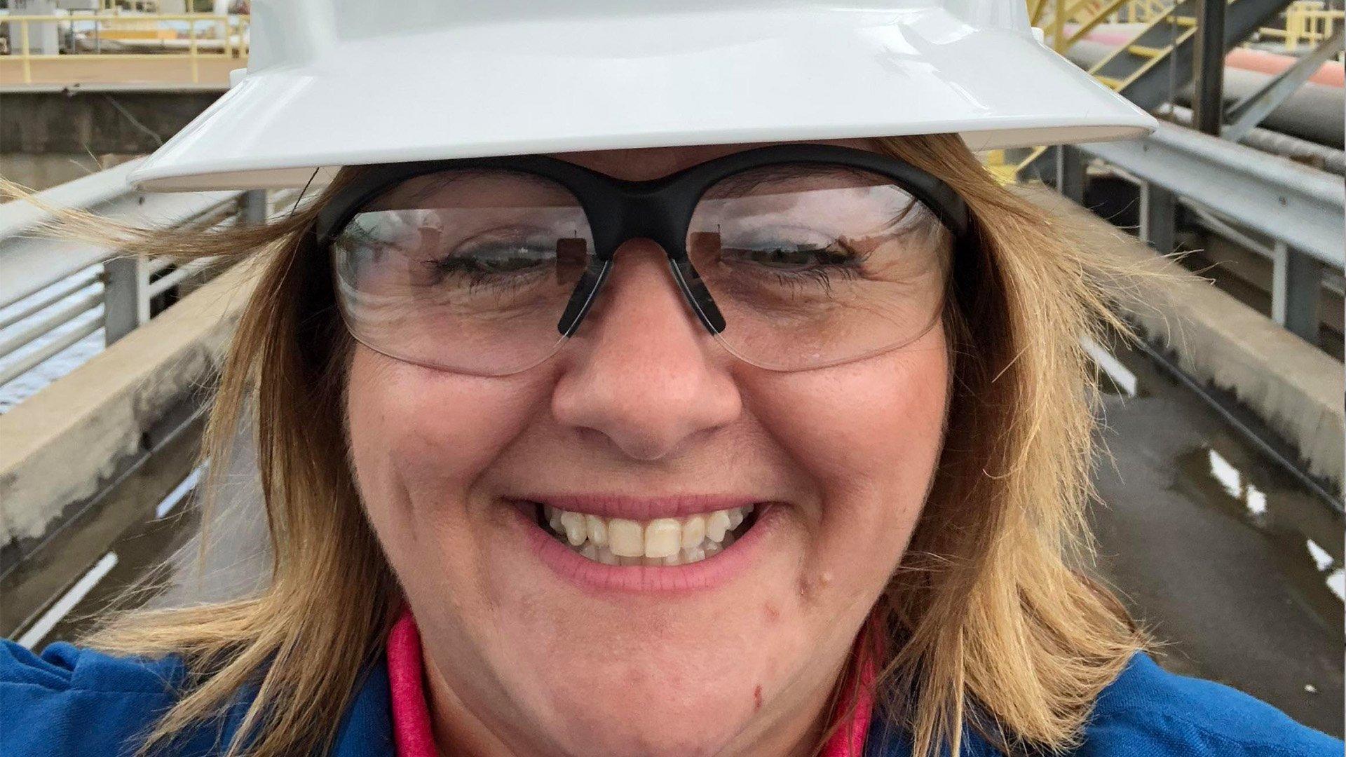 Kathy V, wearing a hard hat and safety glasses, smiles in a selfie taken on a jobsite.