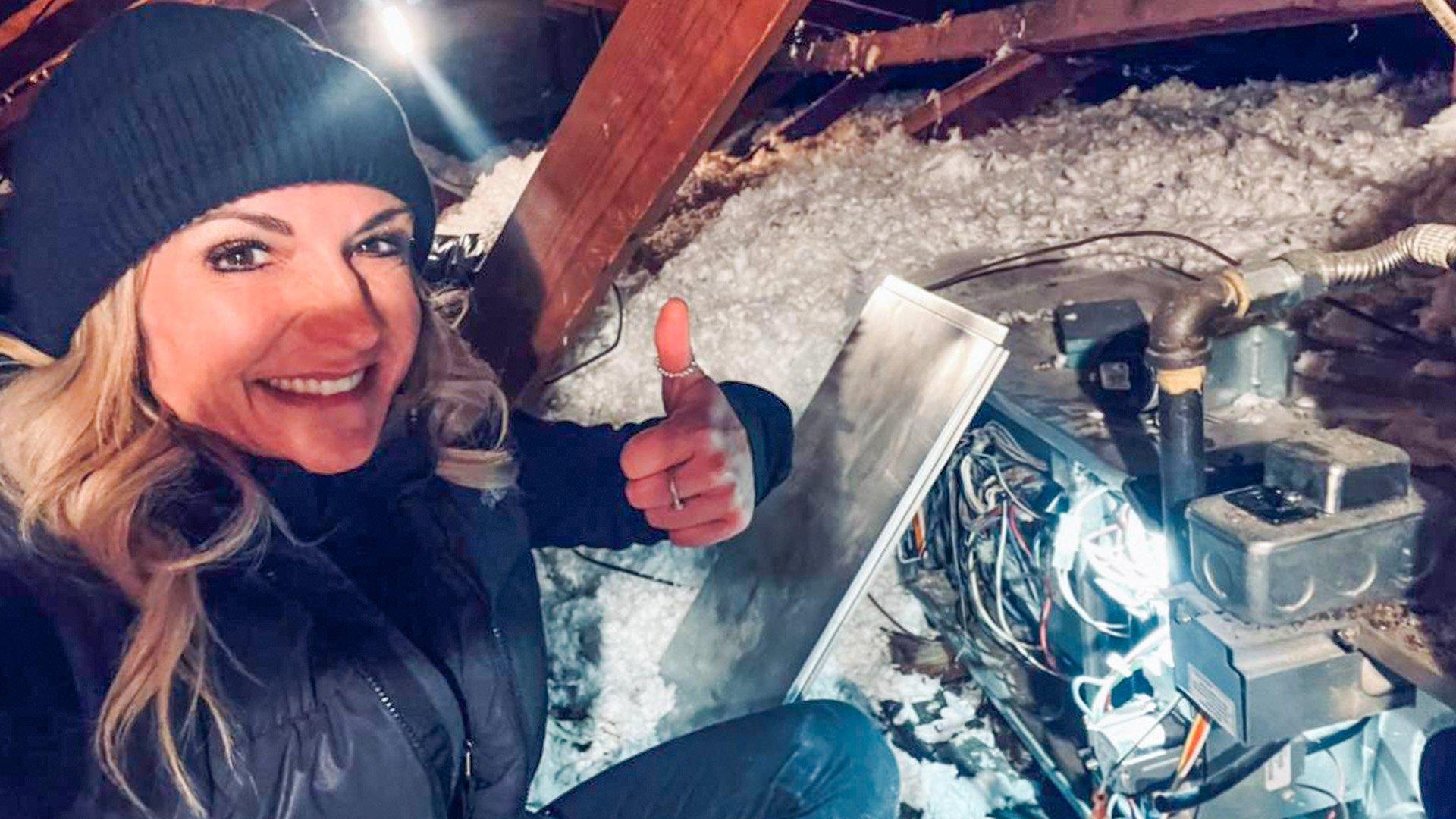 Megan W smiles and gives a thumbs-up next to an HVAC unit in a residential attic.
