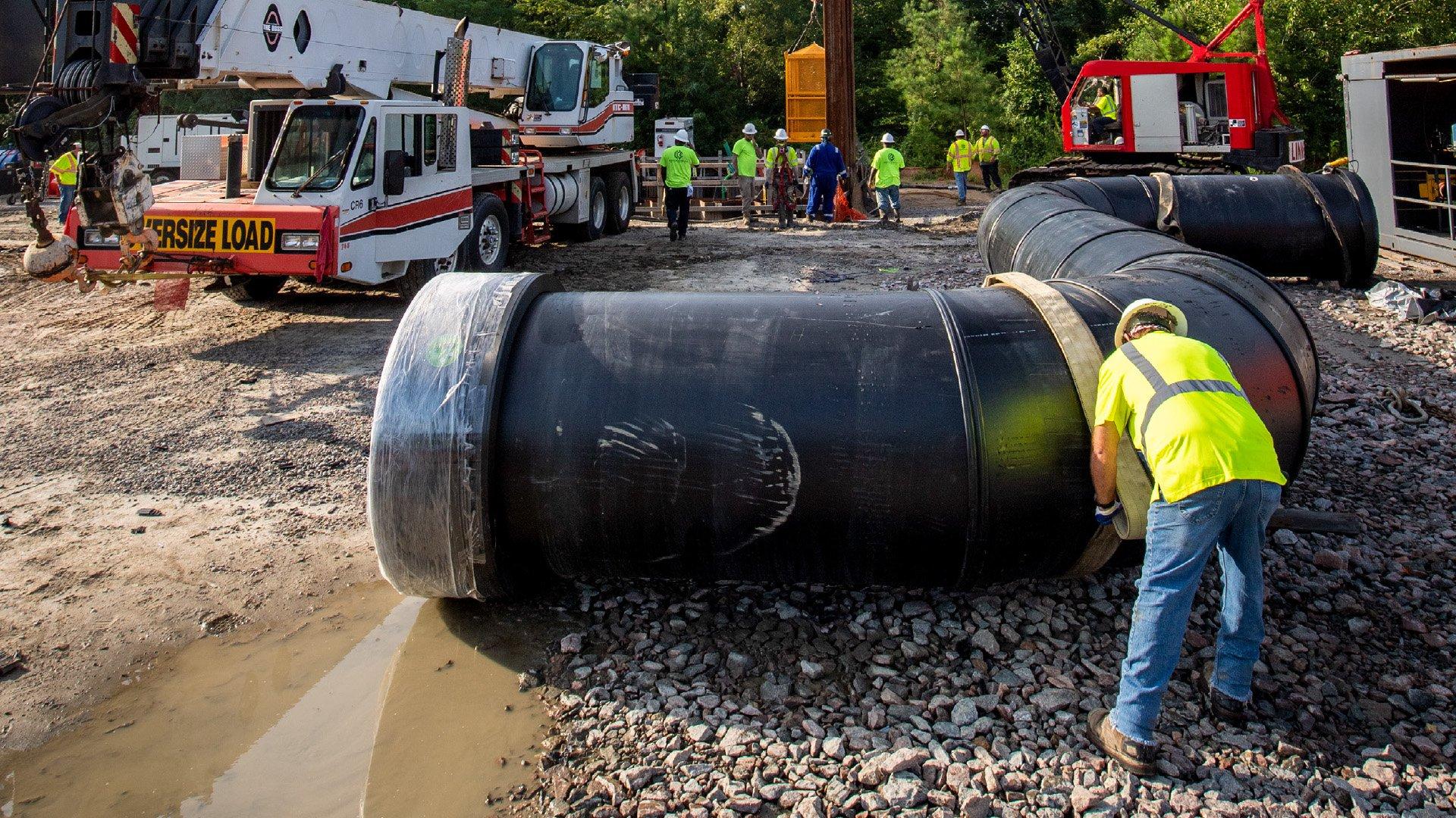 A worker is strapping a large HDPE pipe with crane in the background