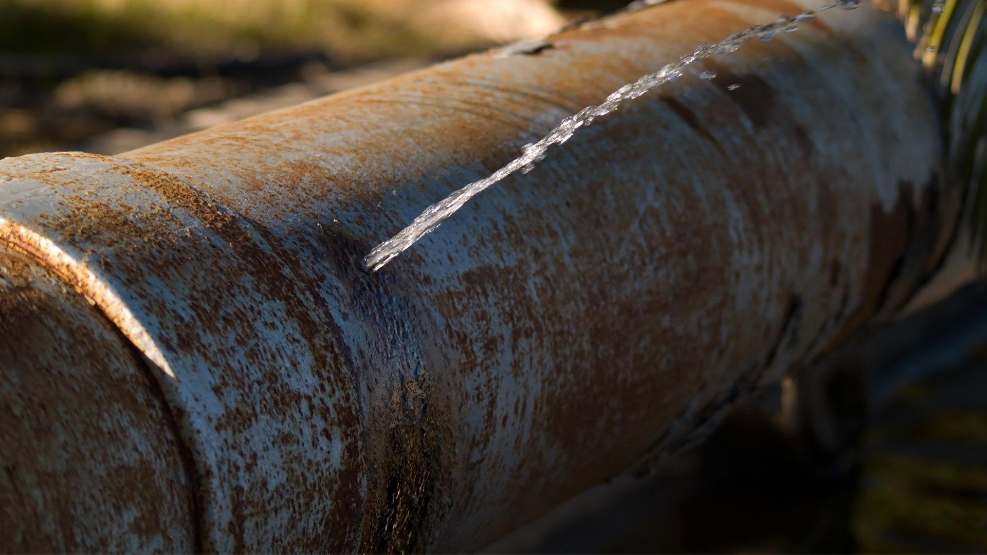 Water sprays out of a leak on a large utility pipe.