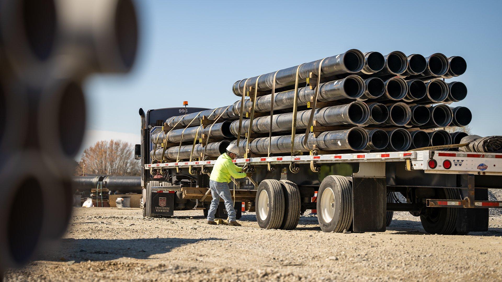 Contractor secures pipes onto large, flatbed truck for delivery to jobsite. 