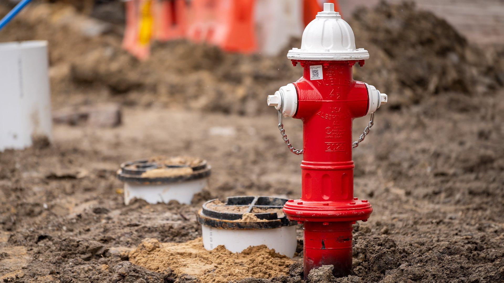 A red fire hydrant with white trim is installed in the ground on a jobsite.