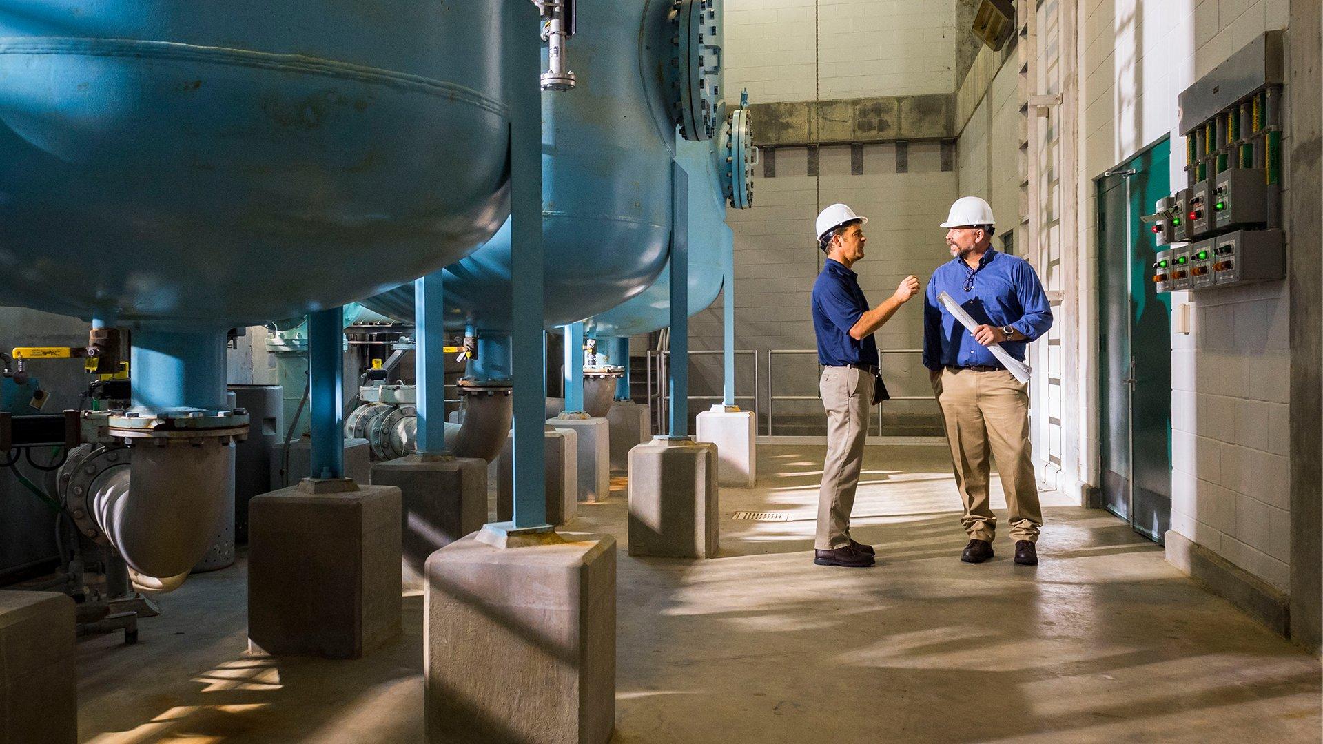 Two men in PPE holding paperwork talking in commercial facility.